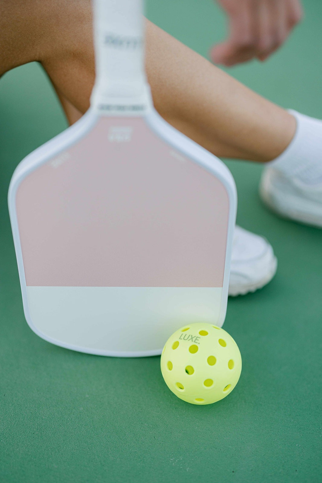 Close-up of a pickleball paddle, pickleball, and white athletic shoes on a green court.