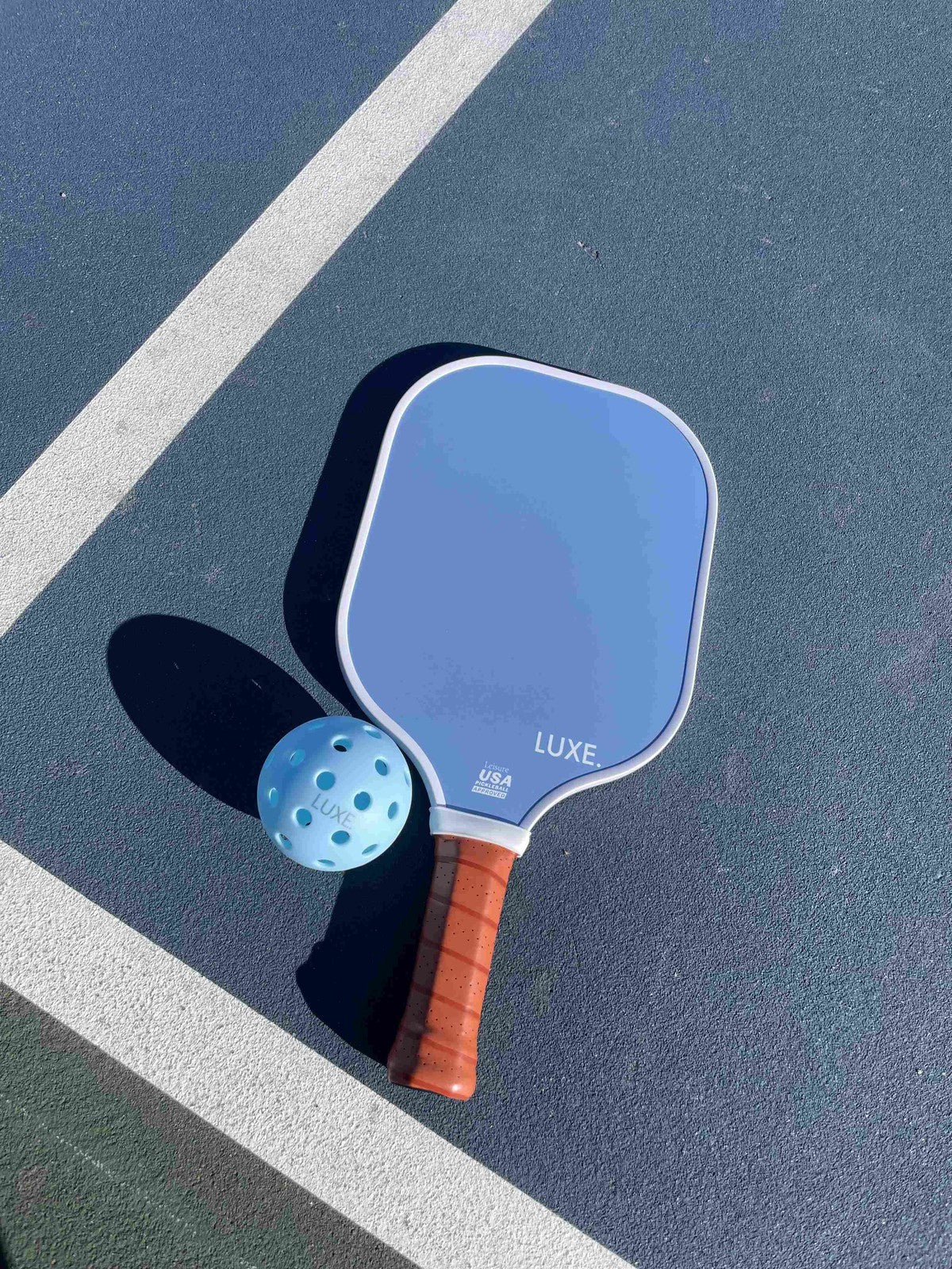 Blue pickleball paddle and ball on a blue court.