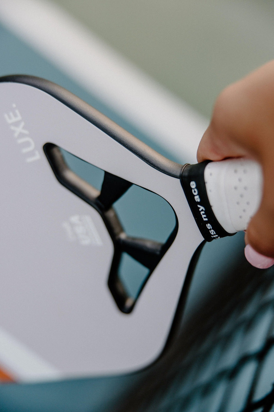 Close-up of hand holding a gray pickleball paddle with a white grip reading "kiss my ace."