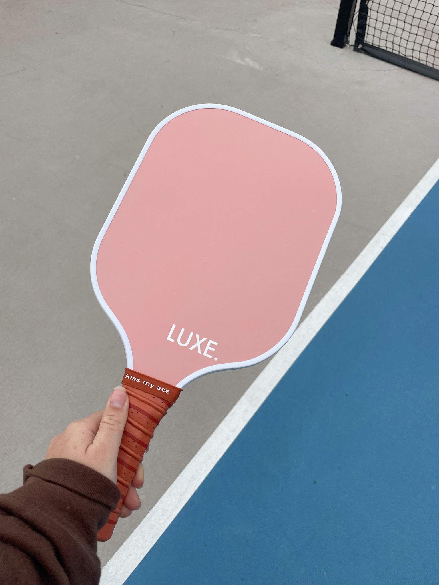 Hand holding pink and brown pickleball paddle on court.