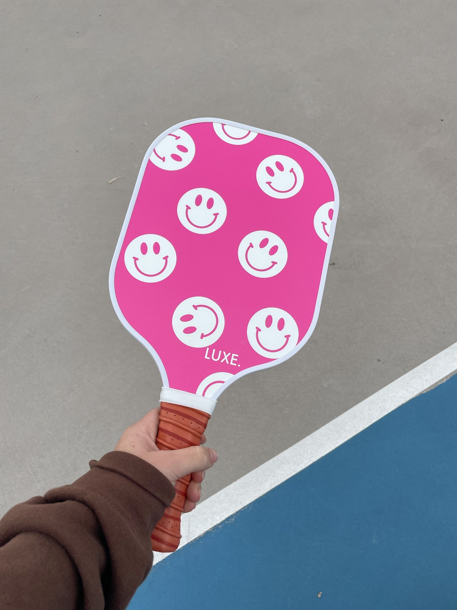 Person holding a pink pickleball paddle with smiley faces.