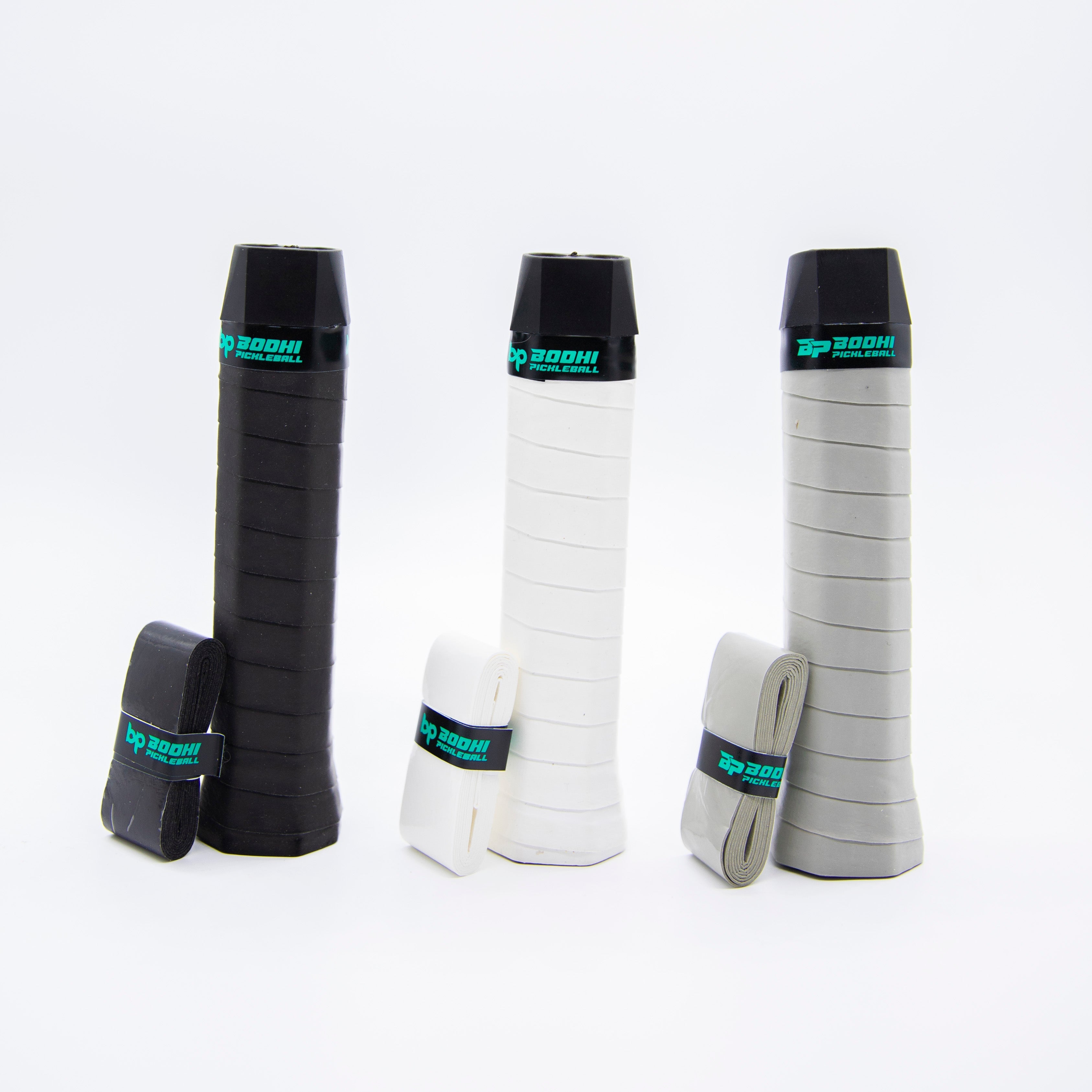 Three pickleball racquet grips, black, white, and gray, with wrapped overgrips.