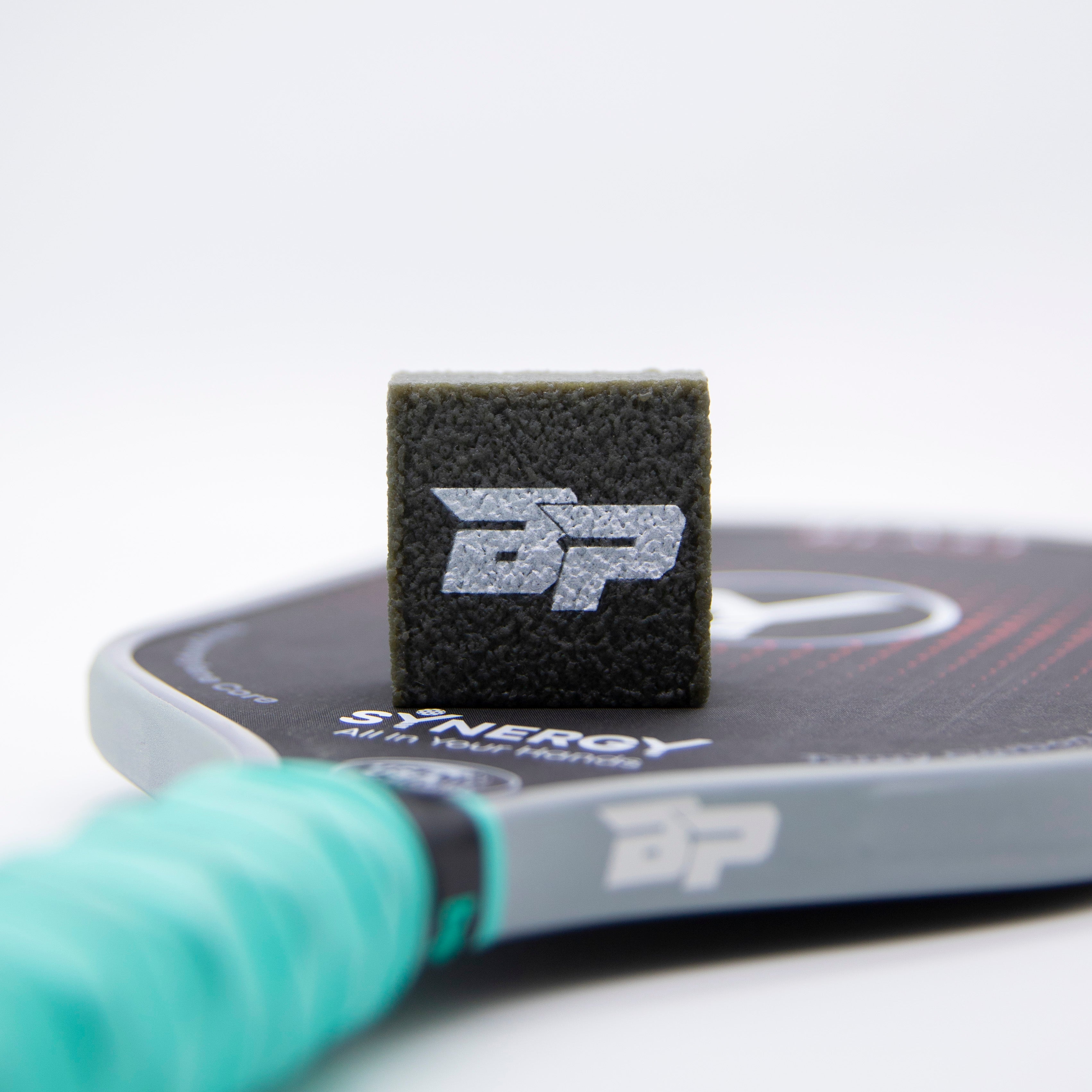 Black block with white logo on pickleball paddle.