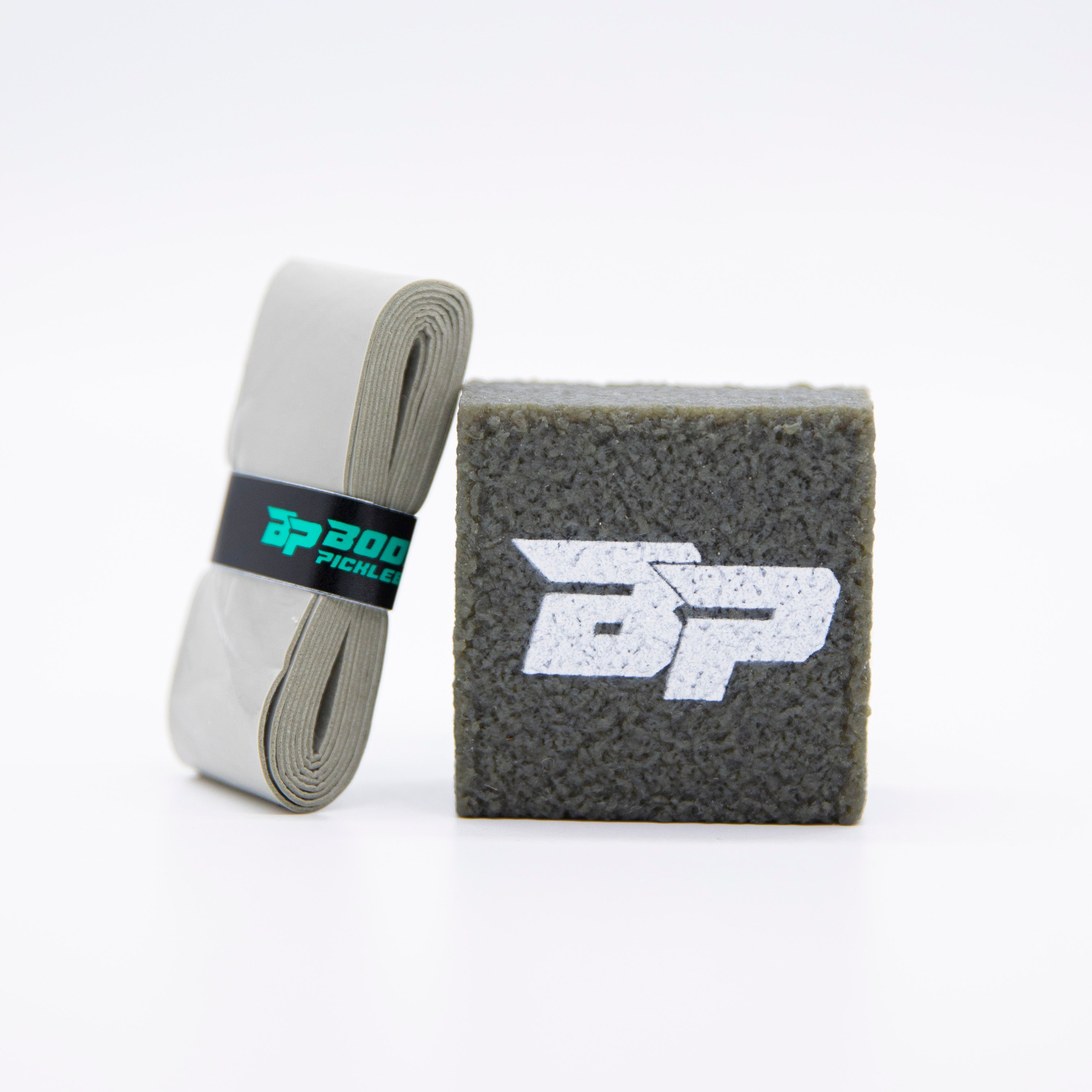Dark grey, textured pickleball paddle cleaner by Bodhi Pickleball with a white BP logo, beside a rolled light grey grip tape.