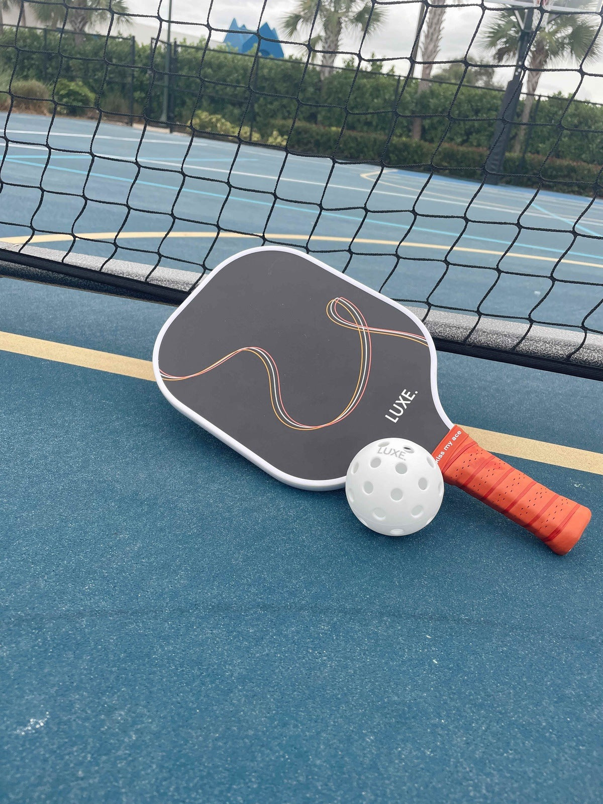 Pickleball paddle and ball on a blue court.