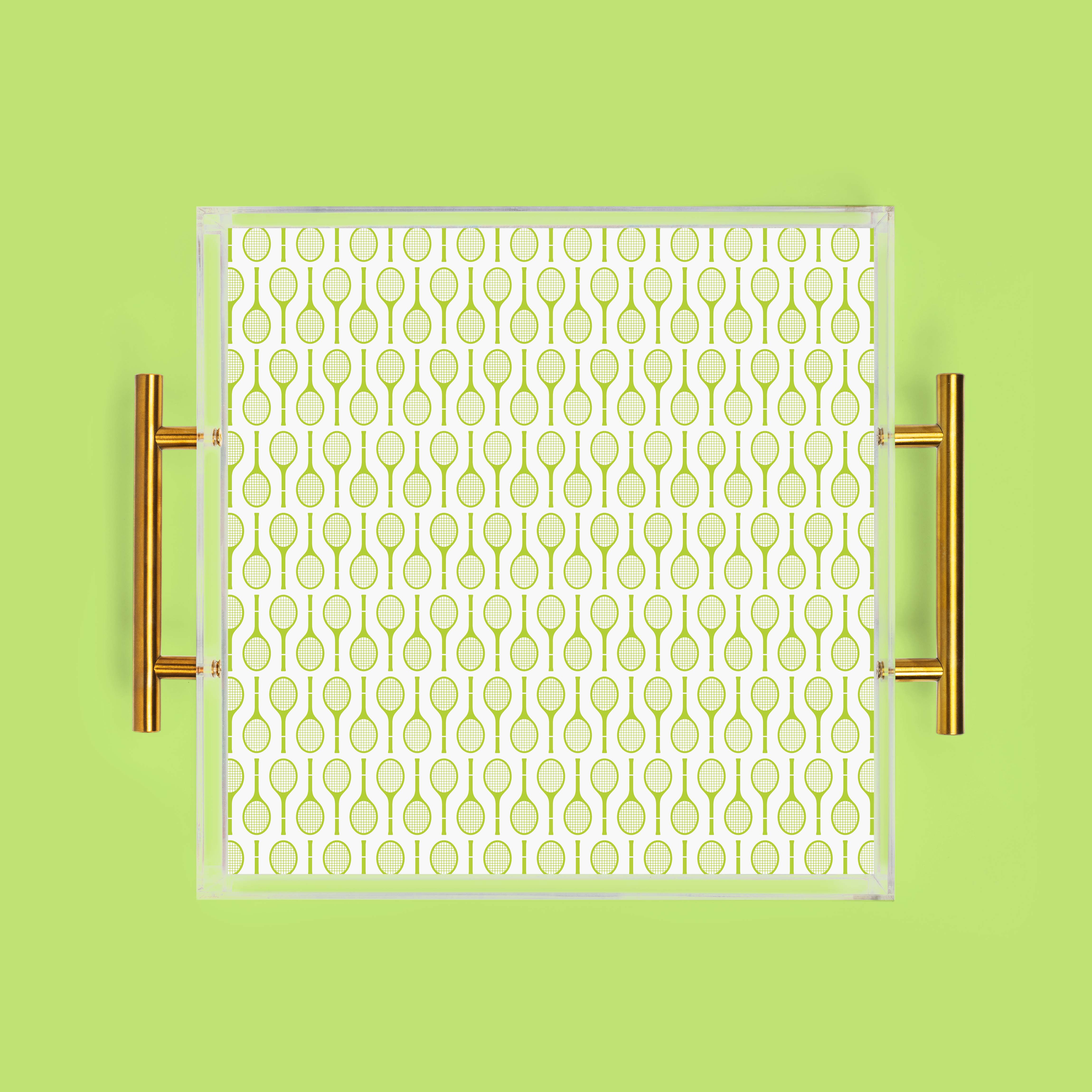 Overhead view of a square clear acrylic tray with gold handles and a green tennis racket pattern on a green background.
