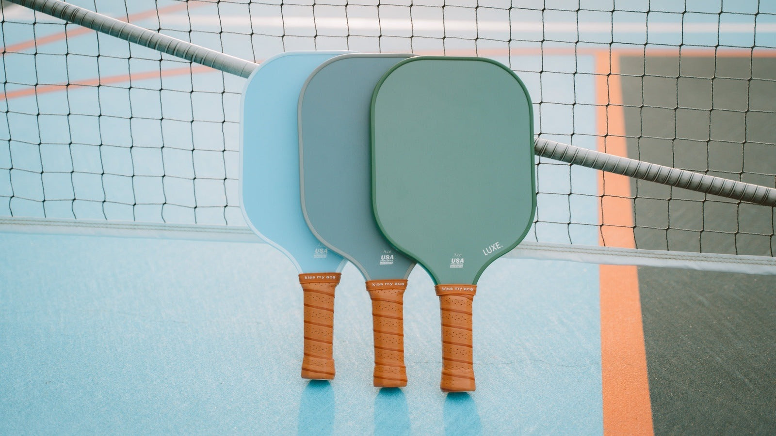 Three pickleball paddles leaning against a net on a blue and green court.
