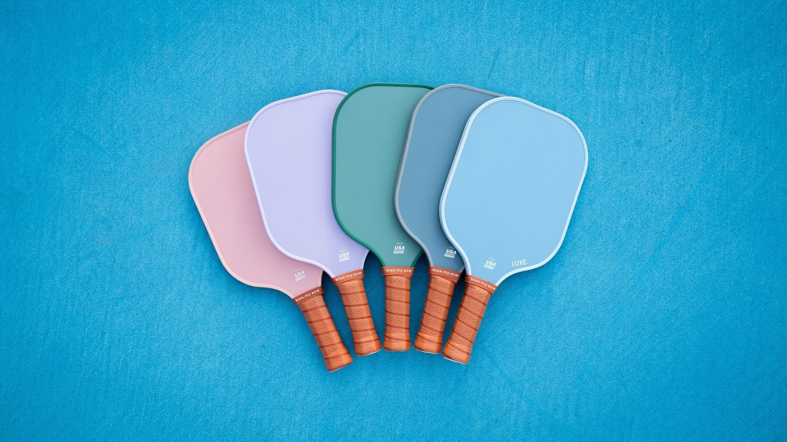 Five colorful pickleball paddles with brown grips on a blue background.