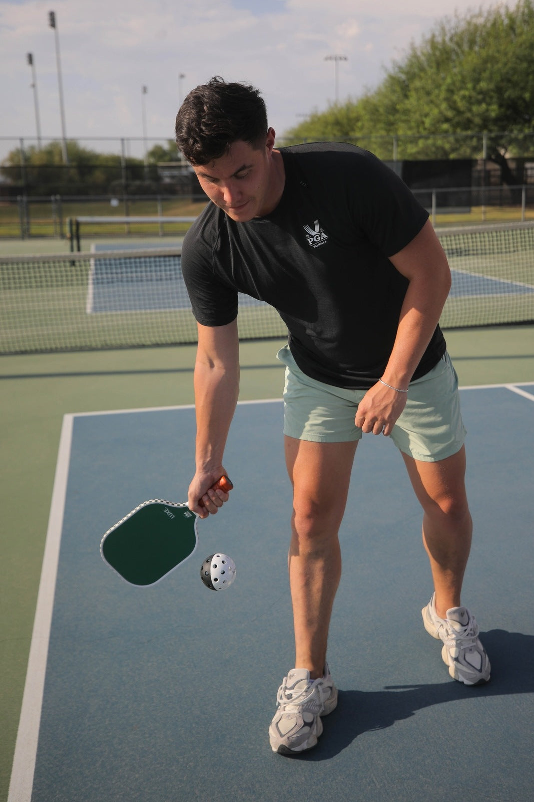 Man in black shirt and green shorts playing pickleball.