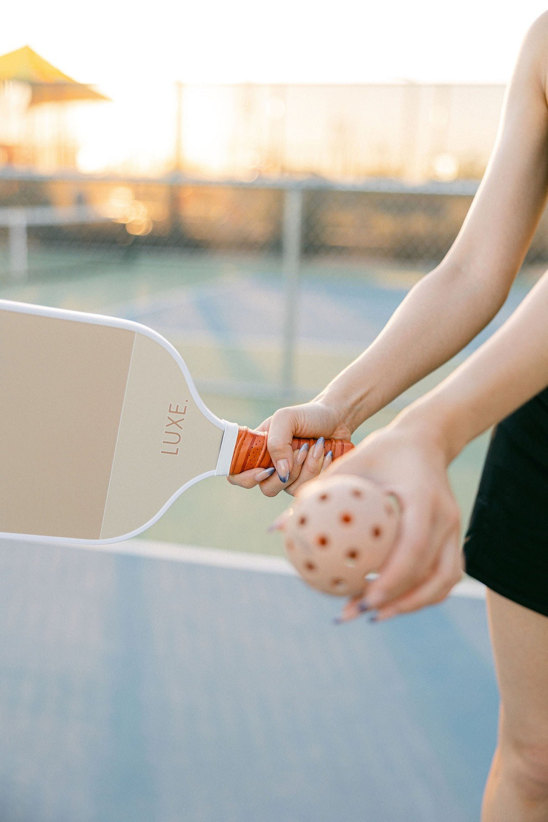 A woman holds a pickleball paddle and a pickleball on a court.