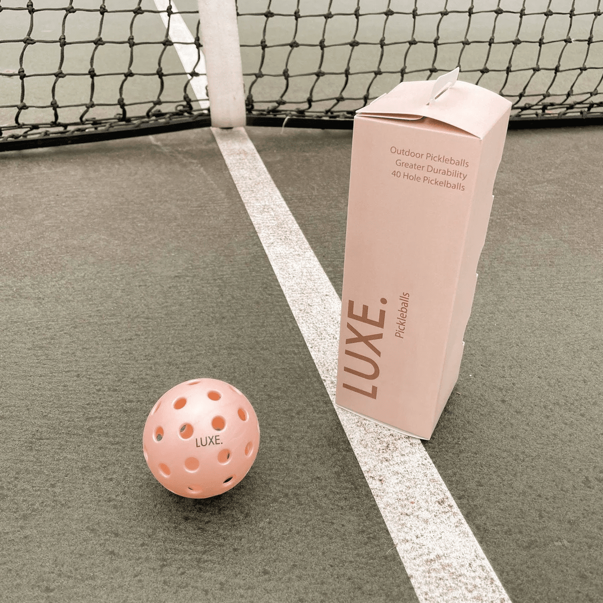Pink pickleball and box of pickleballs on a court.