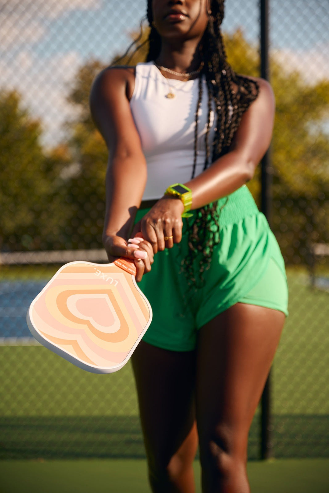 Woman in athletic clothes holding a heart-patterned pickleball paddle on a court.