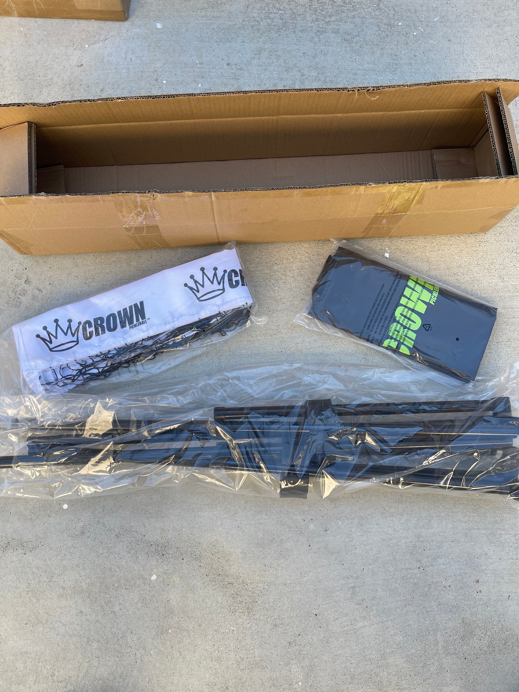 Open cardboard box with packing materials and a disassembled pickleball net.