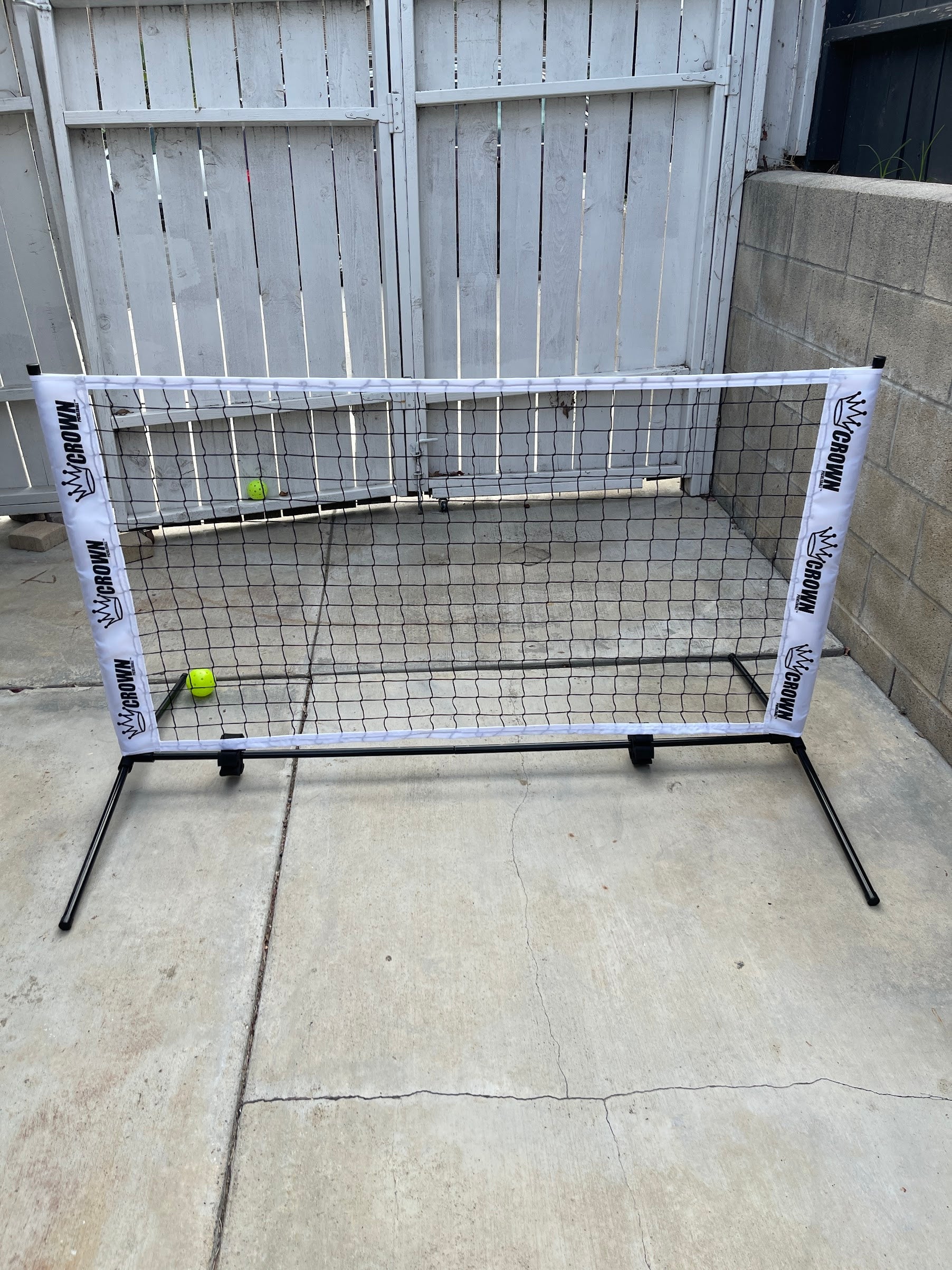 A portable pickleball net with two yellow pickleballs set up in a backyard.
