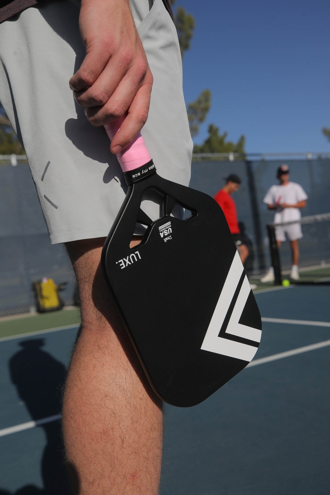 A person holding a black and white pickleball paddle with a pink grip on a blue outdoor court.