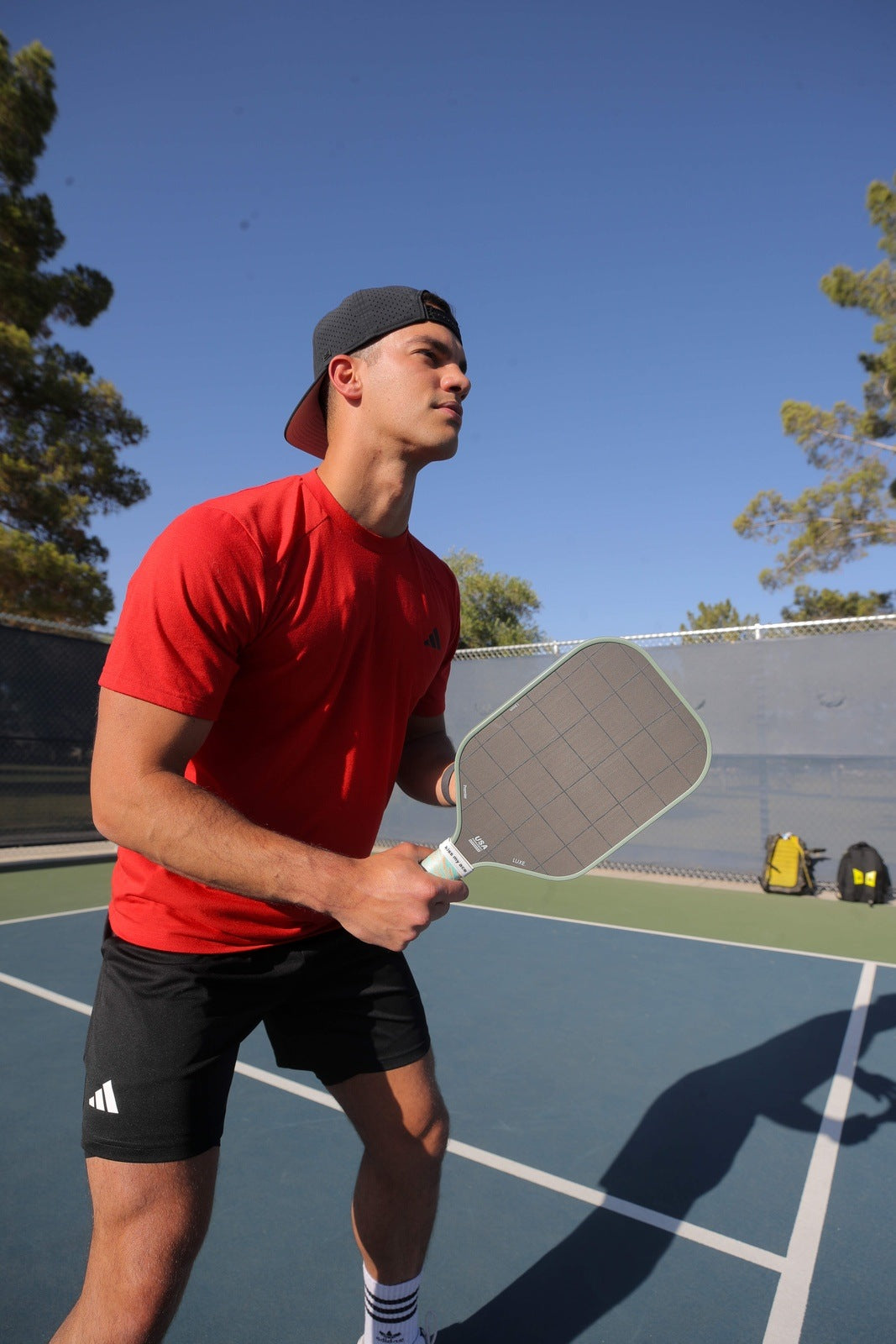 Man on a pickleball court in a red shirt and black shorts holding a pickleball paddle.