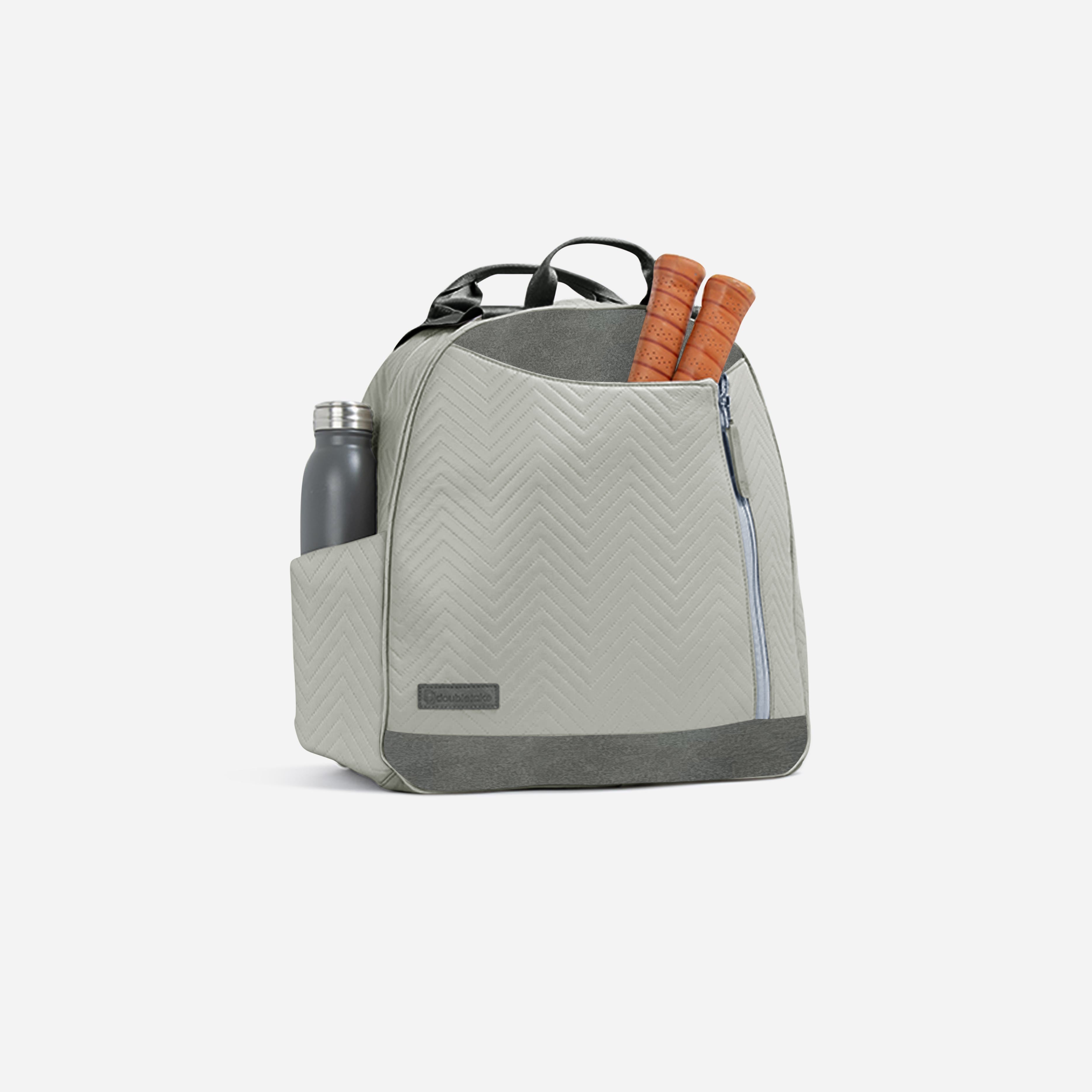 Light grey chevron quilted pickleball backpack and tote by Doubletake, with dark grey accents, a water bottle, and two paddle handles.