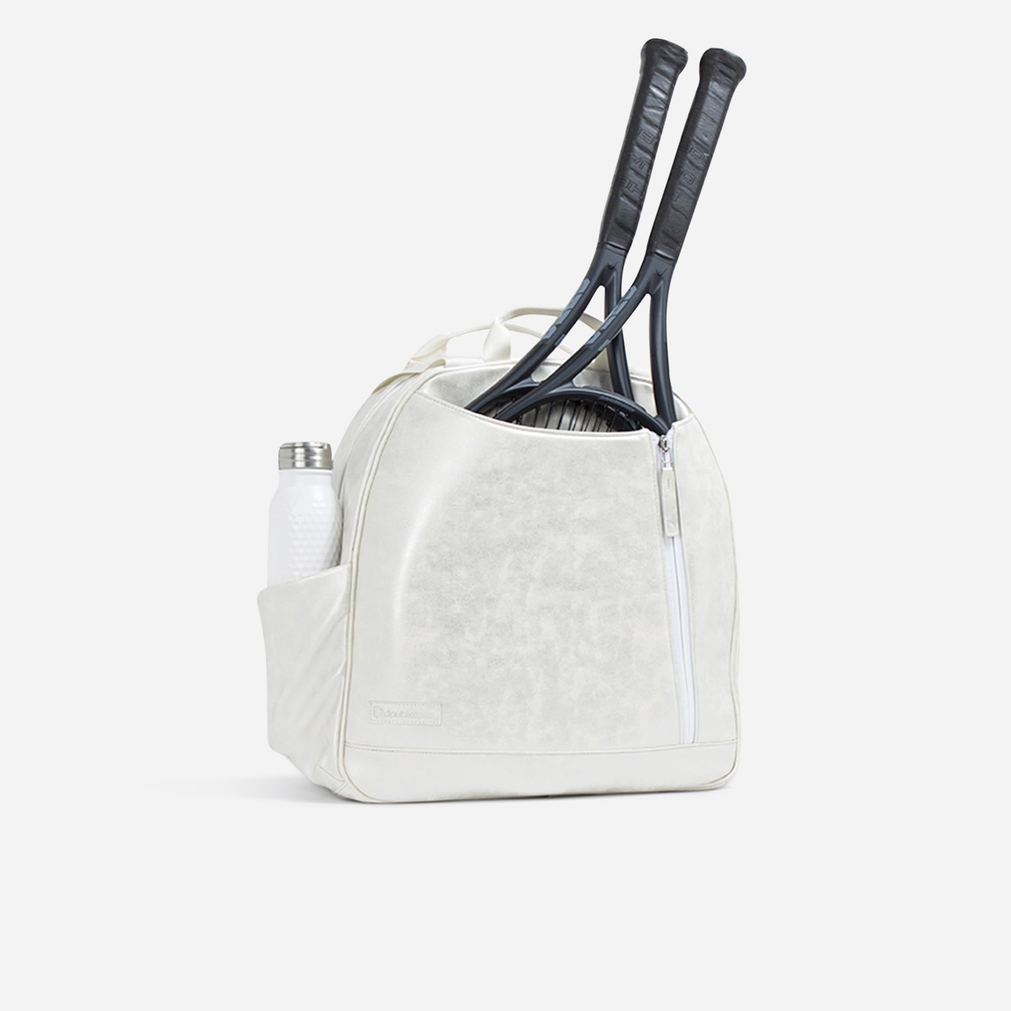 White textured tennis backpack and tote by Doubletake, holding two black tennis rackets and a white water bottle, side view.