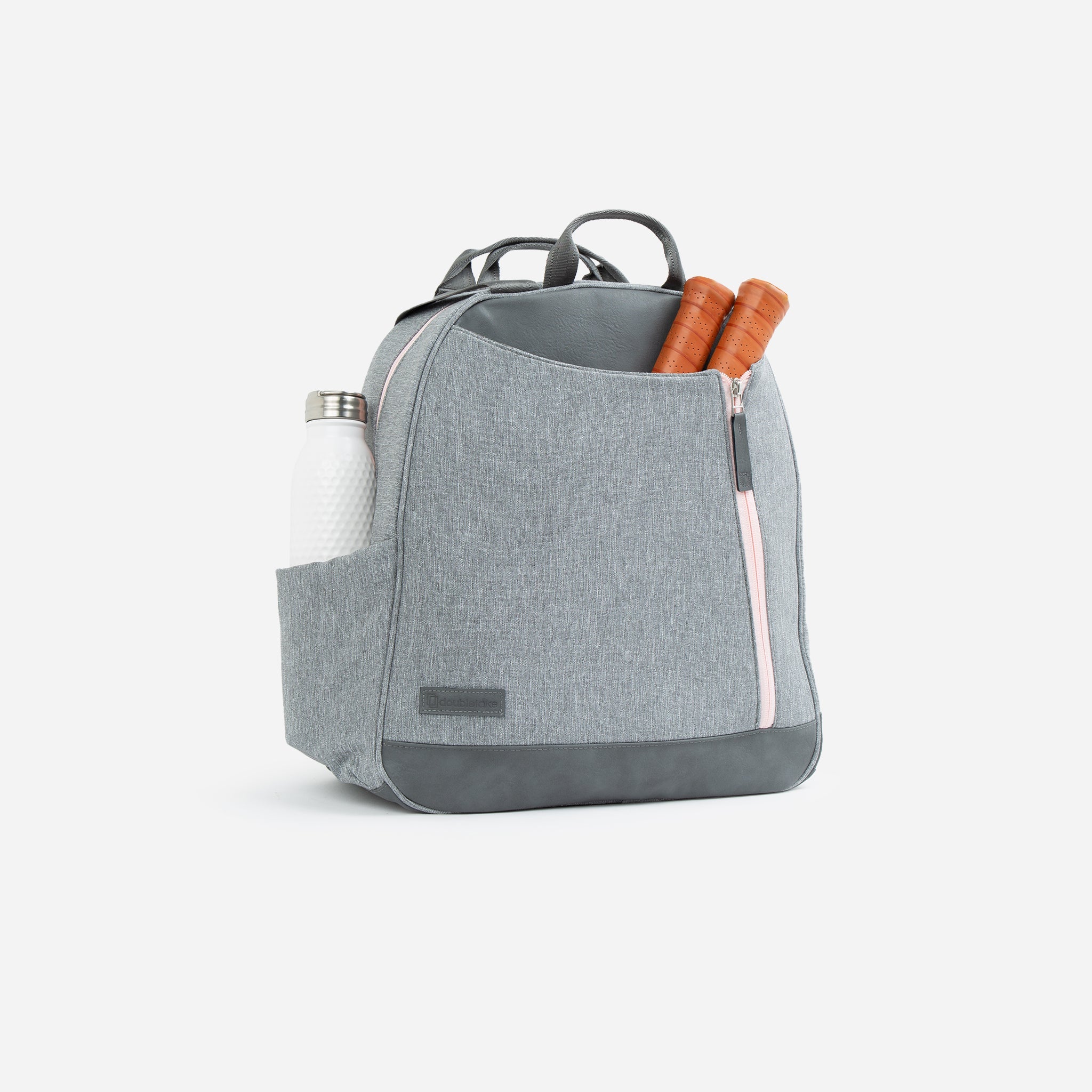 Grey pickleball backpack and tote by Doubletake with pink zippers, holding a white water bottle and orange paddle handles.
