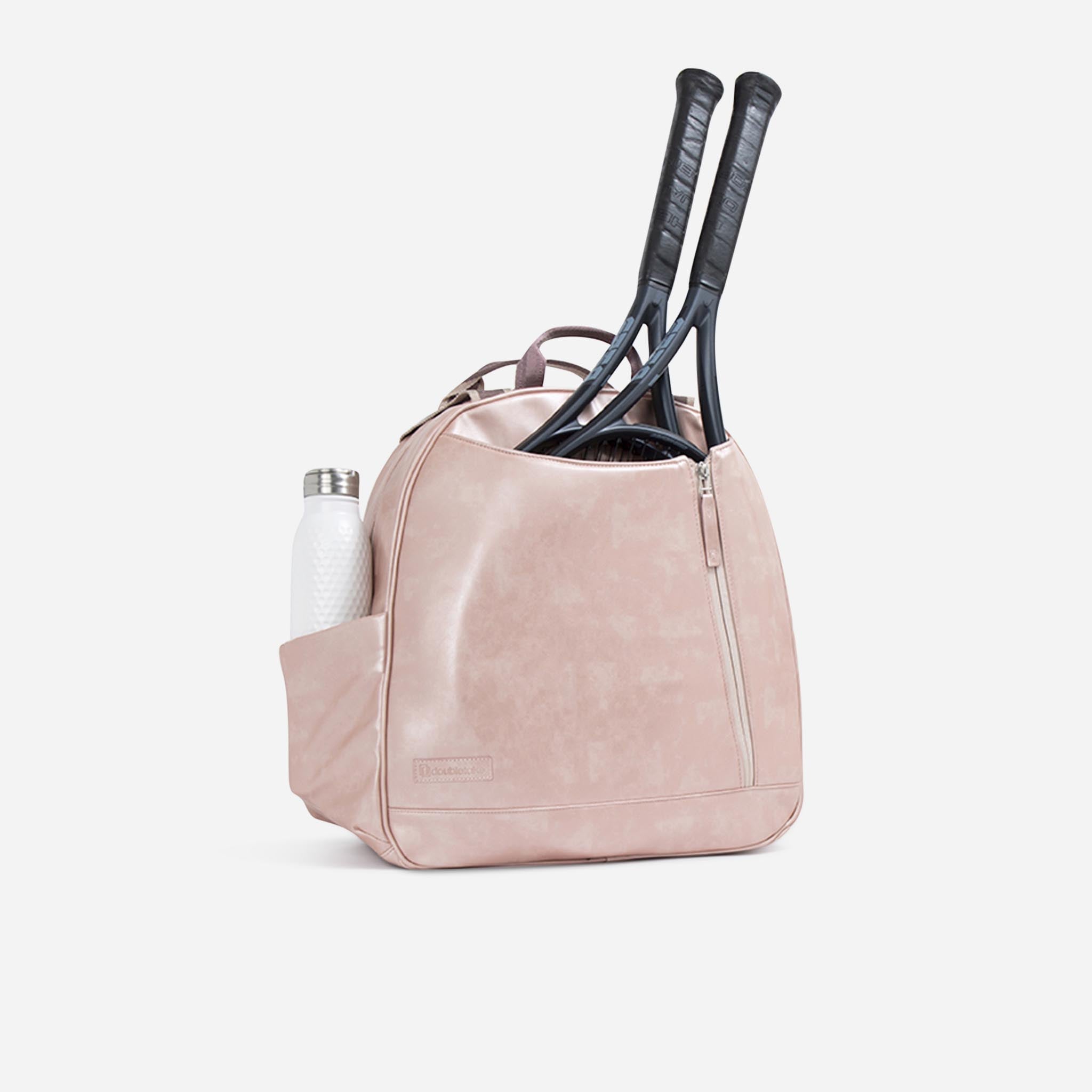 Blush pink tennis backpack and tote by Doubletake, holding two black rackets and a white textured water bottle.