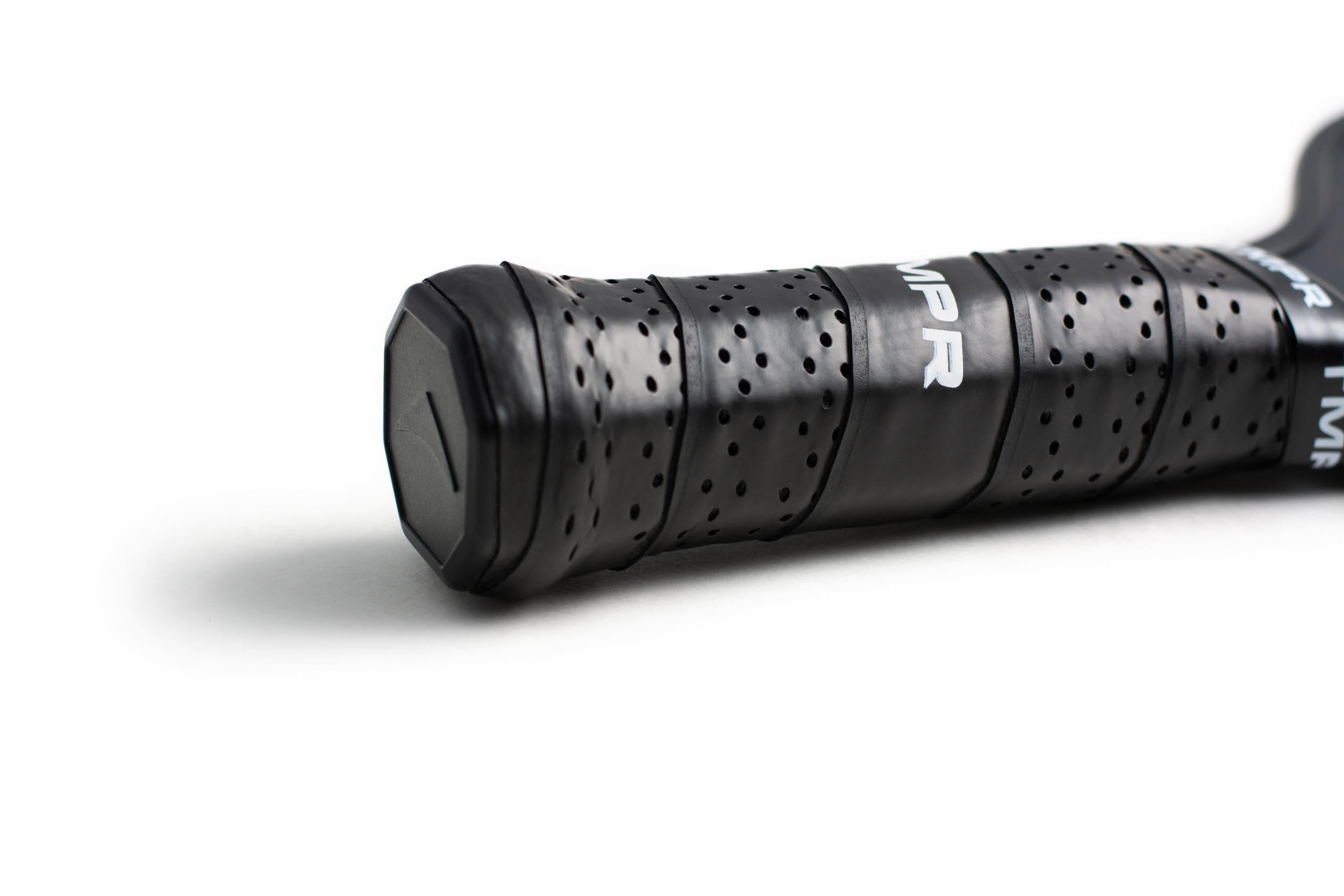 Black perforated pickleball paddle grip by TMPR Sports, with "MPR" lettering and a hexagonal end cap, close-up.