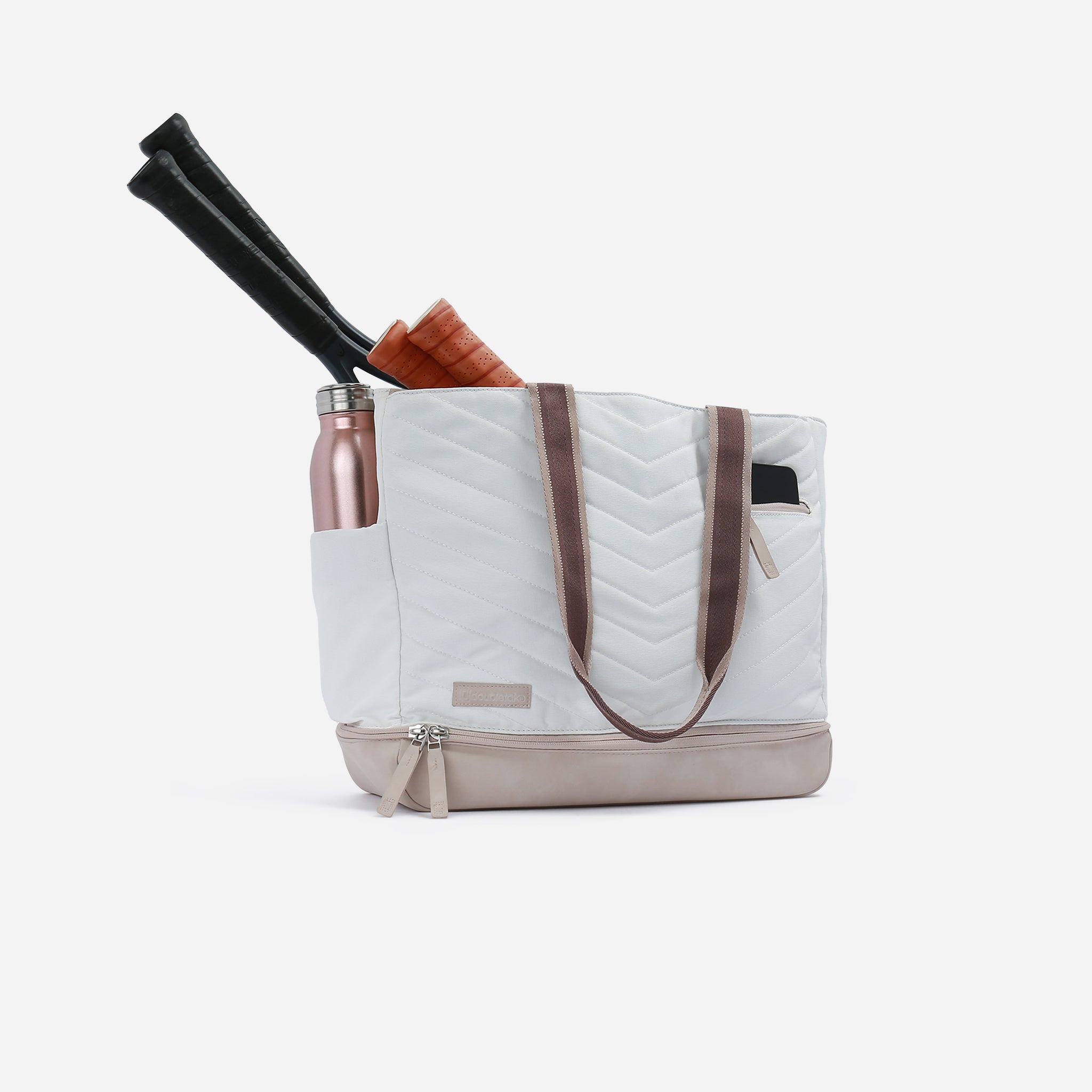 White chevron-quilted tennis tote by Doubletake, with brown straps, holding a rose gold water bottle and two tennis rackets, angled.