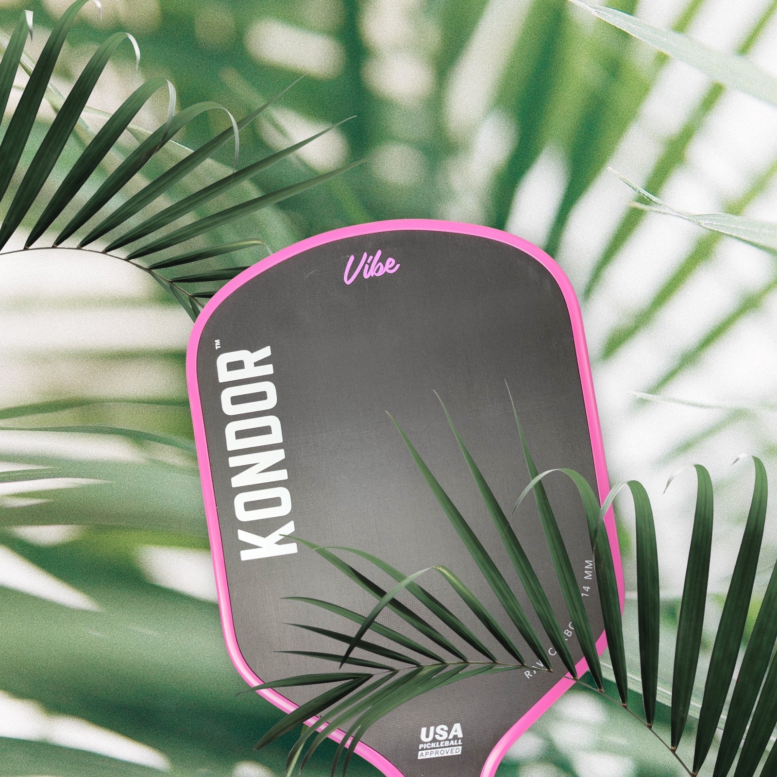 Black pickleball paddle with pink trim by KONDOR PICKLEBALL, featuring 'Vibe' text, surrounded by tropical palm leaves.