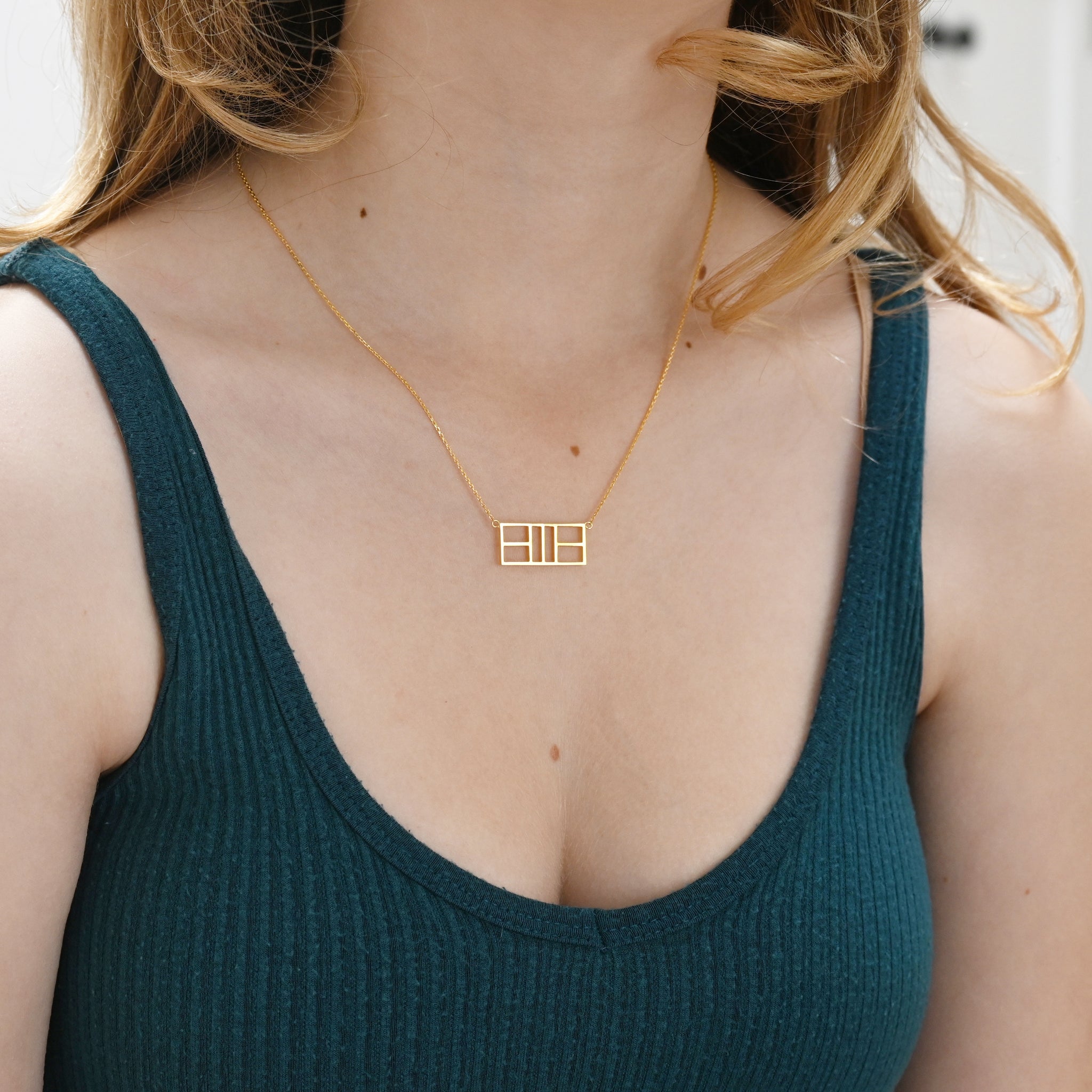 A woman wearing a gold necklace and a ribbed, teal top.