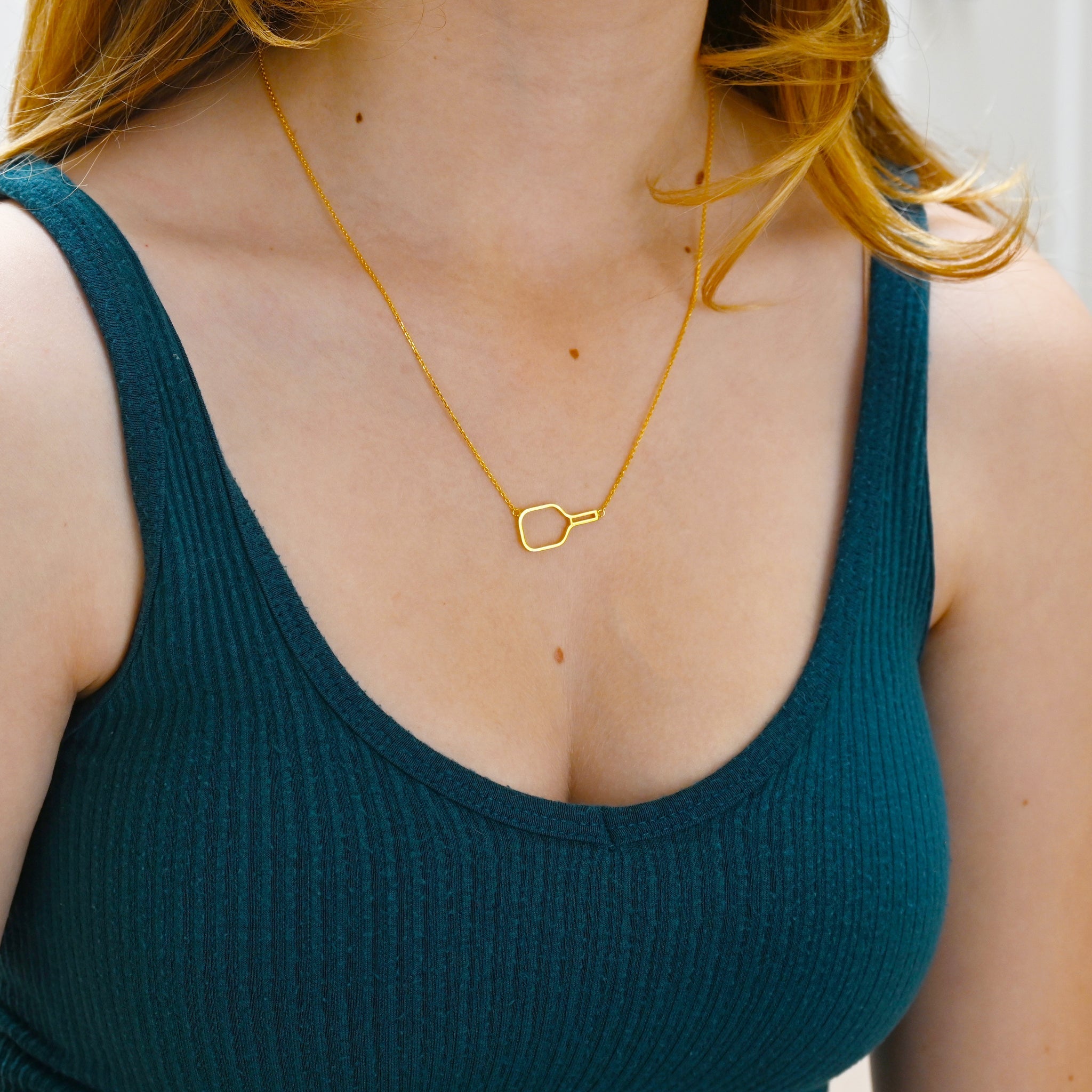 Woman wearing a green tank top and a gold pickleball paddle necklace.
