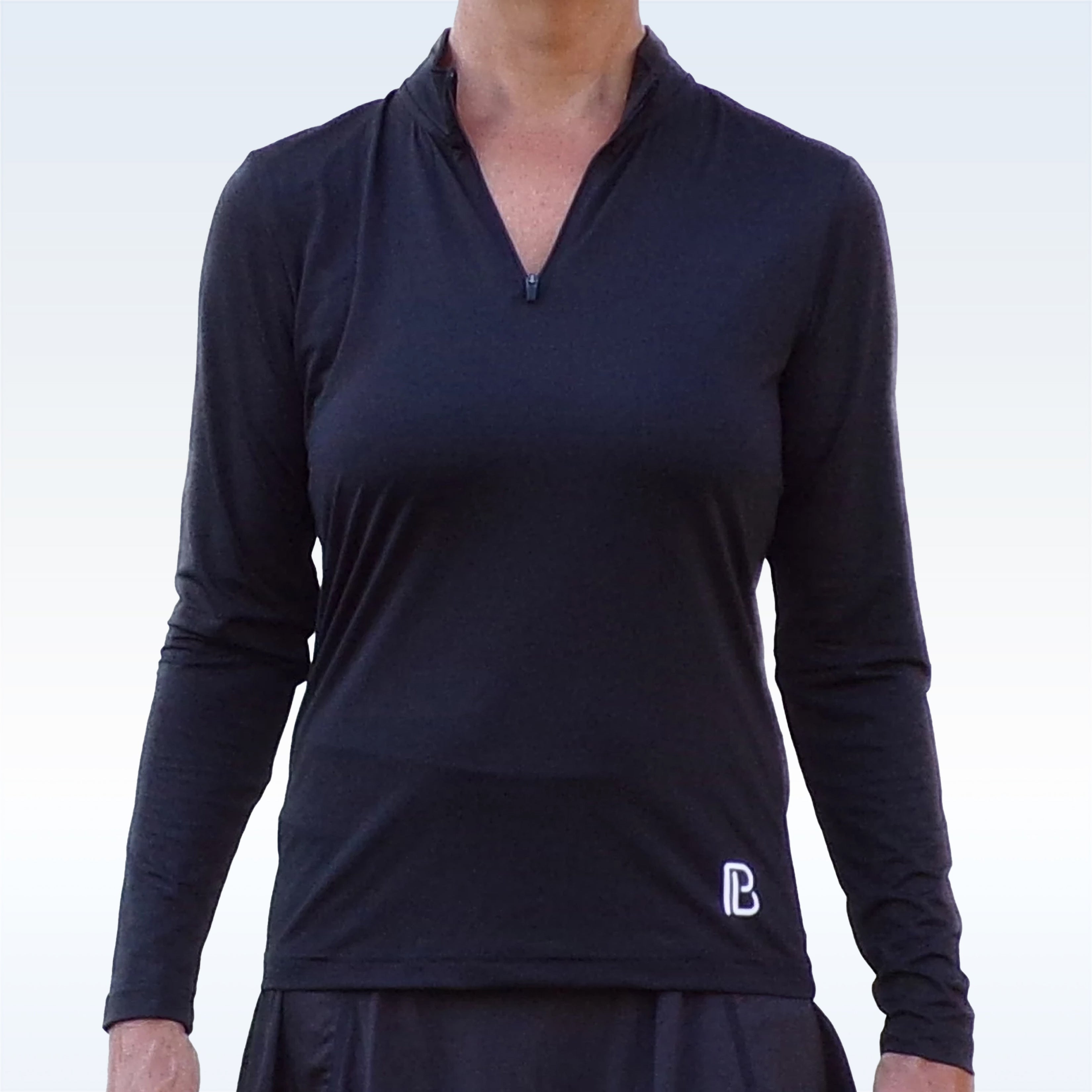 Black 1/4 zip long sleeve pullover by Pickleball Bella with a white PB logo, styled with a black skirt.
