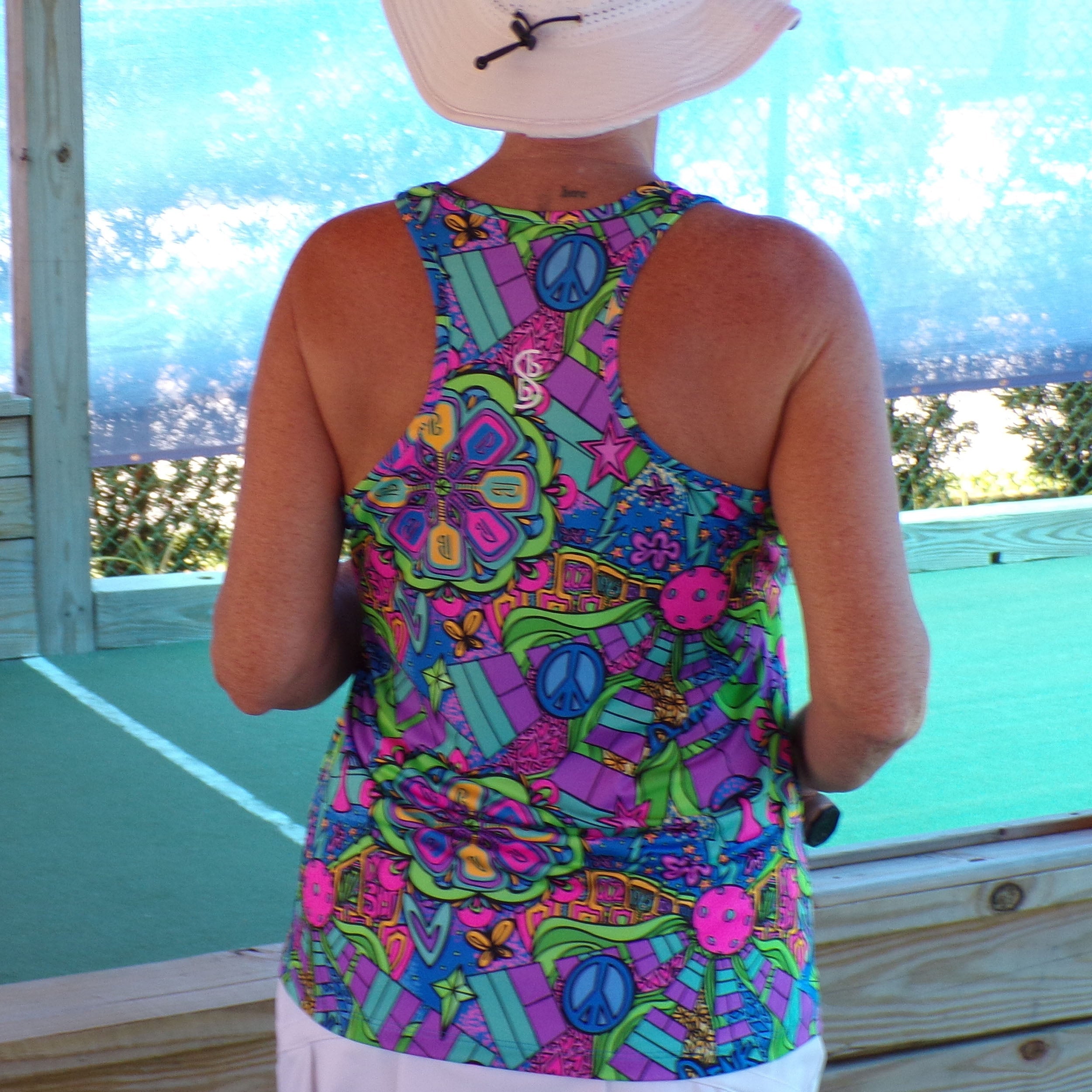 Racerback tank by Pickleball Bella with a vibrant multi-colored groovy pattern featuring peace signs, stars, and flowers, worn from the back.