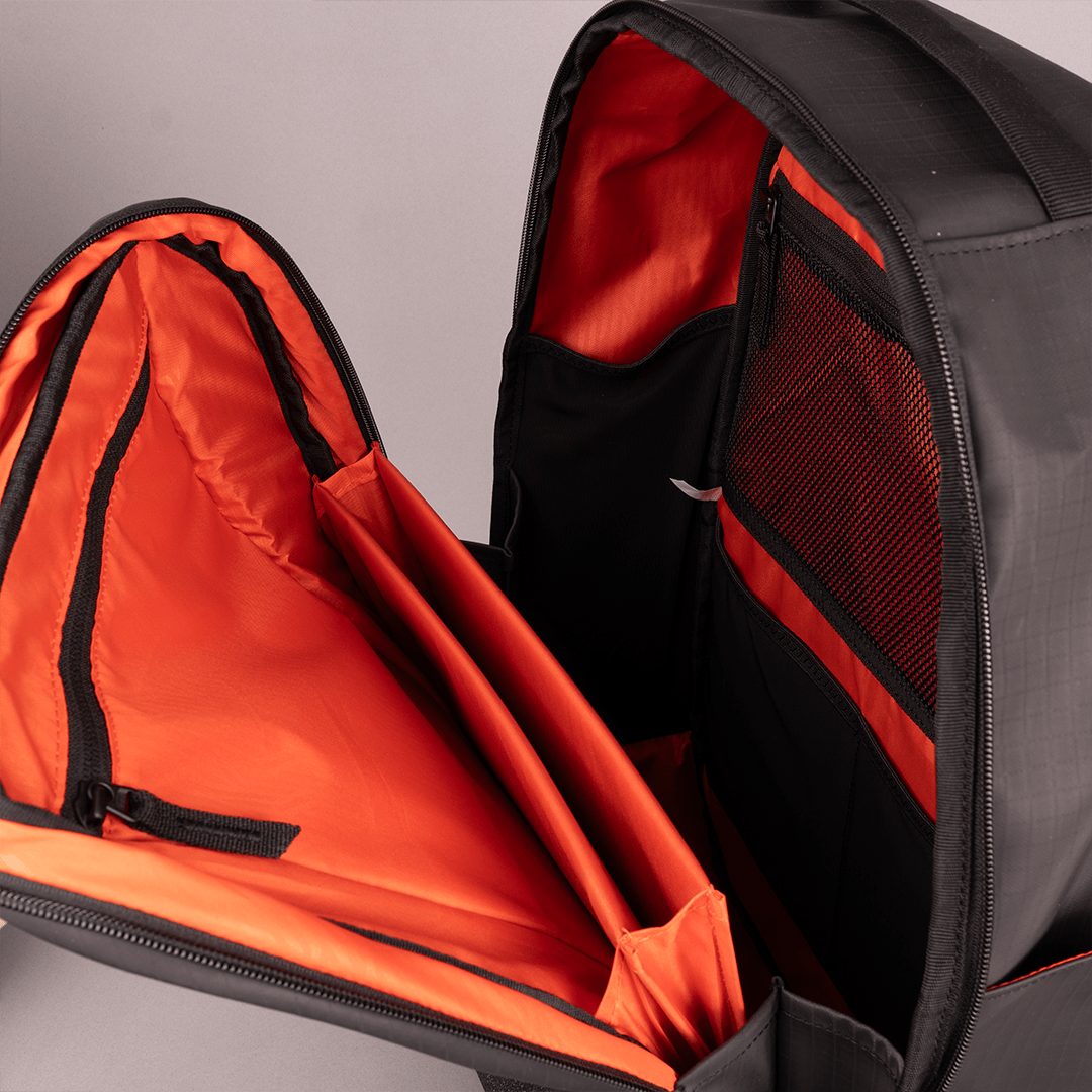 Black pickleball backpack by FORWRD, open to reveal bright orange interior lining with multiple pockets and a mesh compartment.