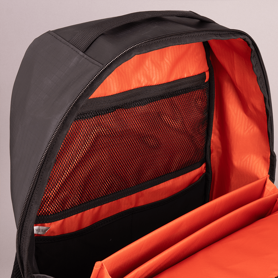 Black pickleball backpack with orange interior by FORWRD, open to reveal a mesh pocket and multiple storage compartments.