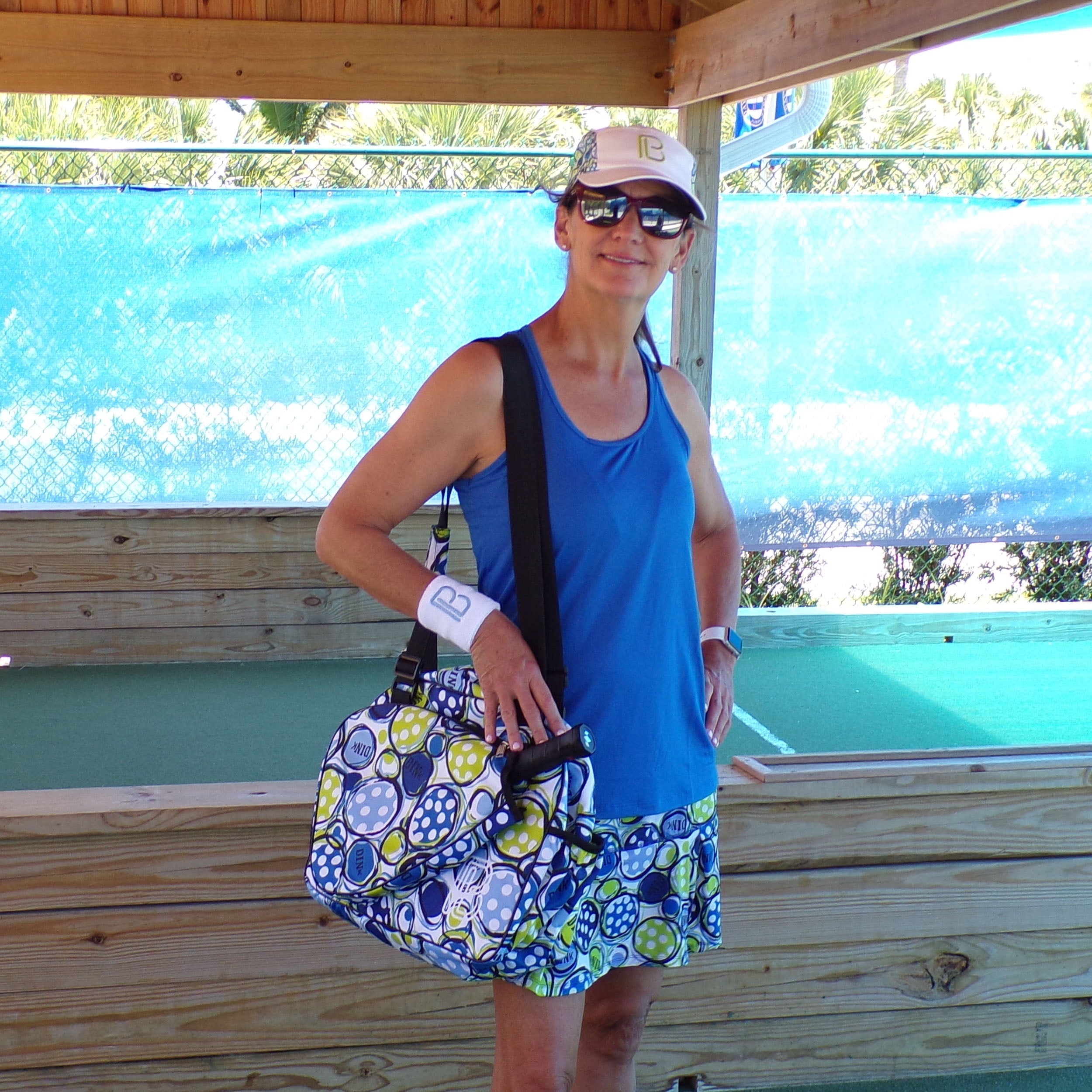 Royal blue racerback tank by Pickleball Bella, worn by a woman holding a paddle, paired with a polka dot skirt.