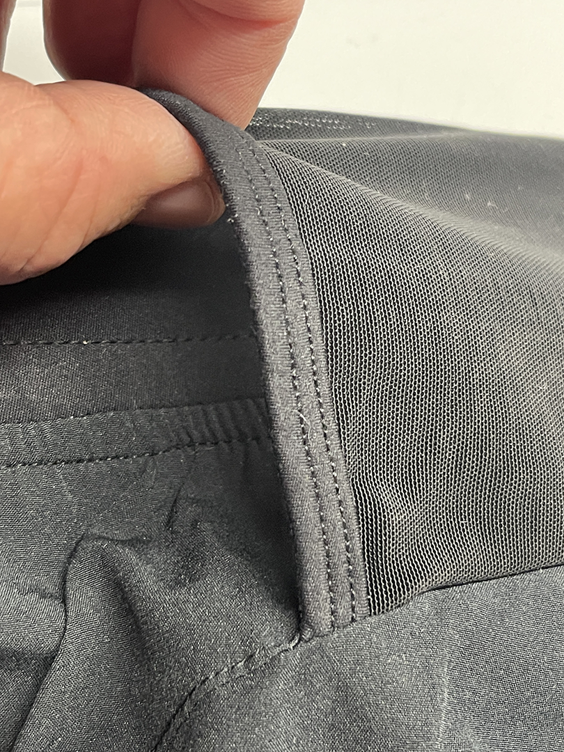 Close-up of gray garment with mesh panel and finger holding up the seam.