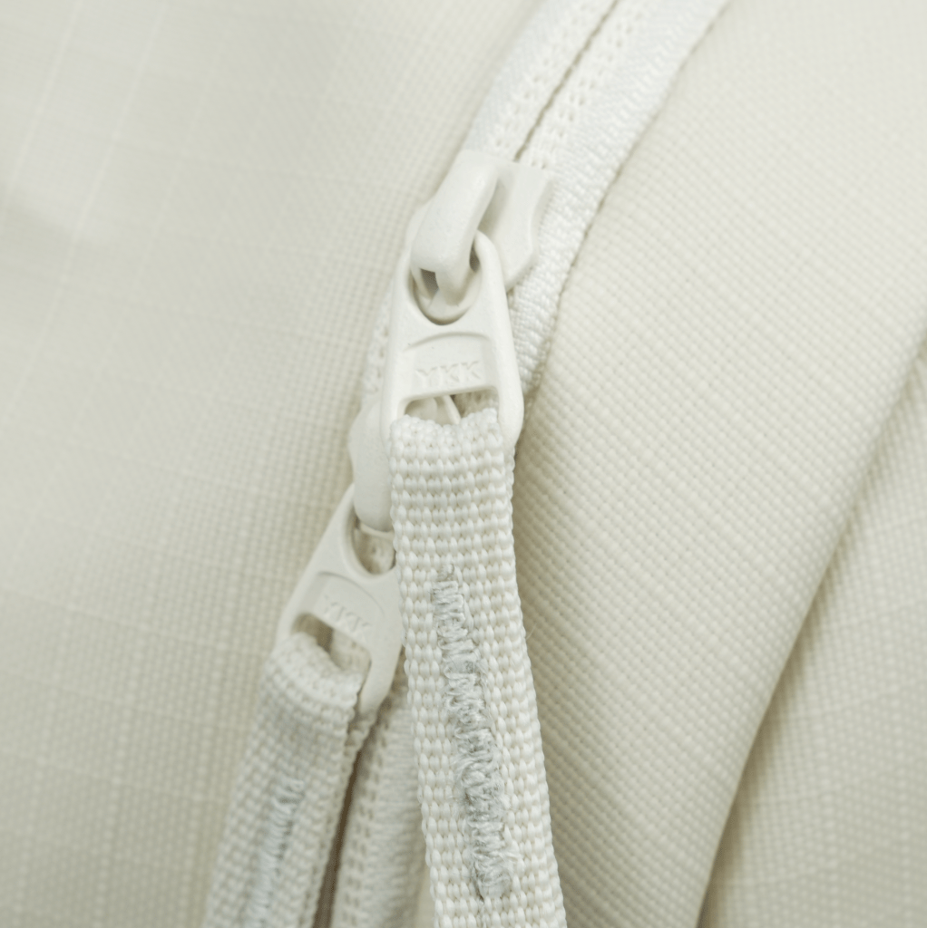 A light beige pickleball backpack by FORWRD, showing a close-up of two white YKK zippers and fabric texture.