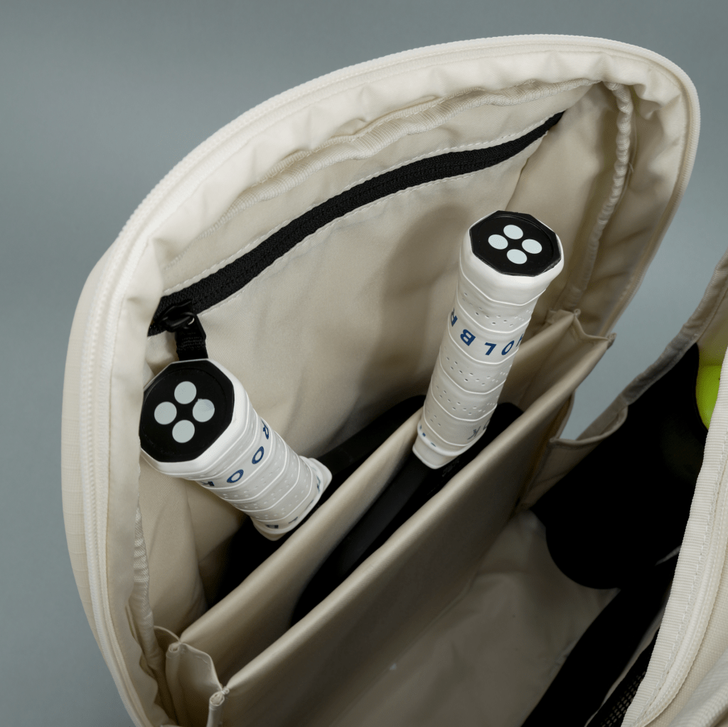 White pickleball backpack by FORWRD, open, revealing internal pockets and two rackets with white and black grips.
