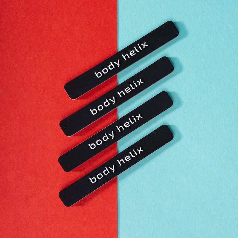 Four black "body helix" nail files on a red and turquoise surface.