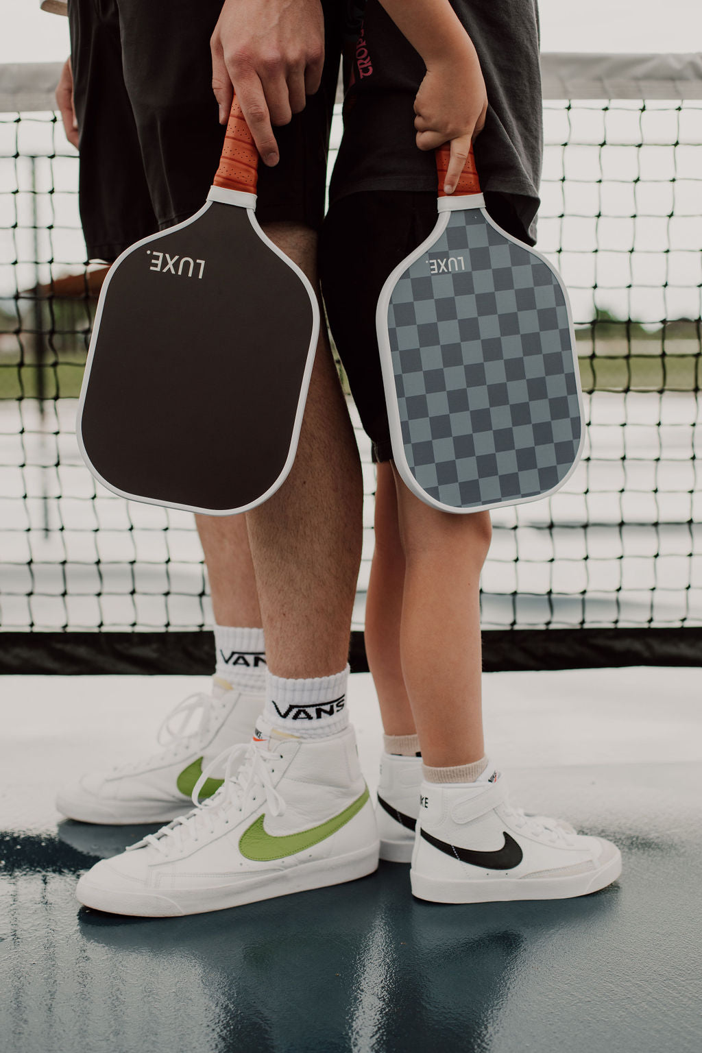 Two people holding pickleball paddles, wearing Nike Blazer shoes and Vans socks on a court.