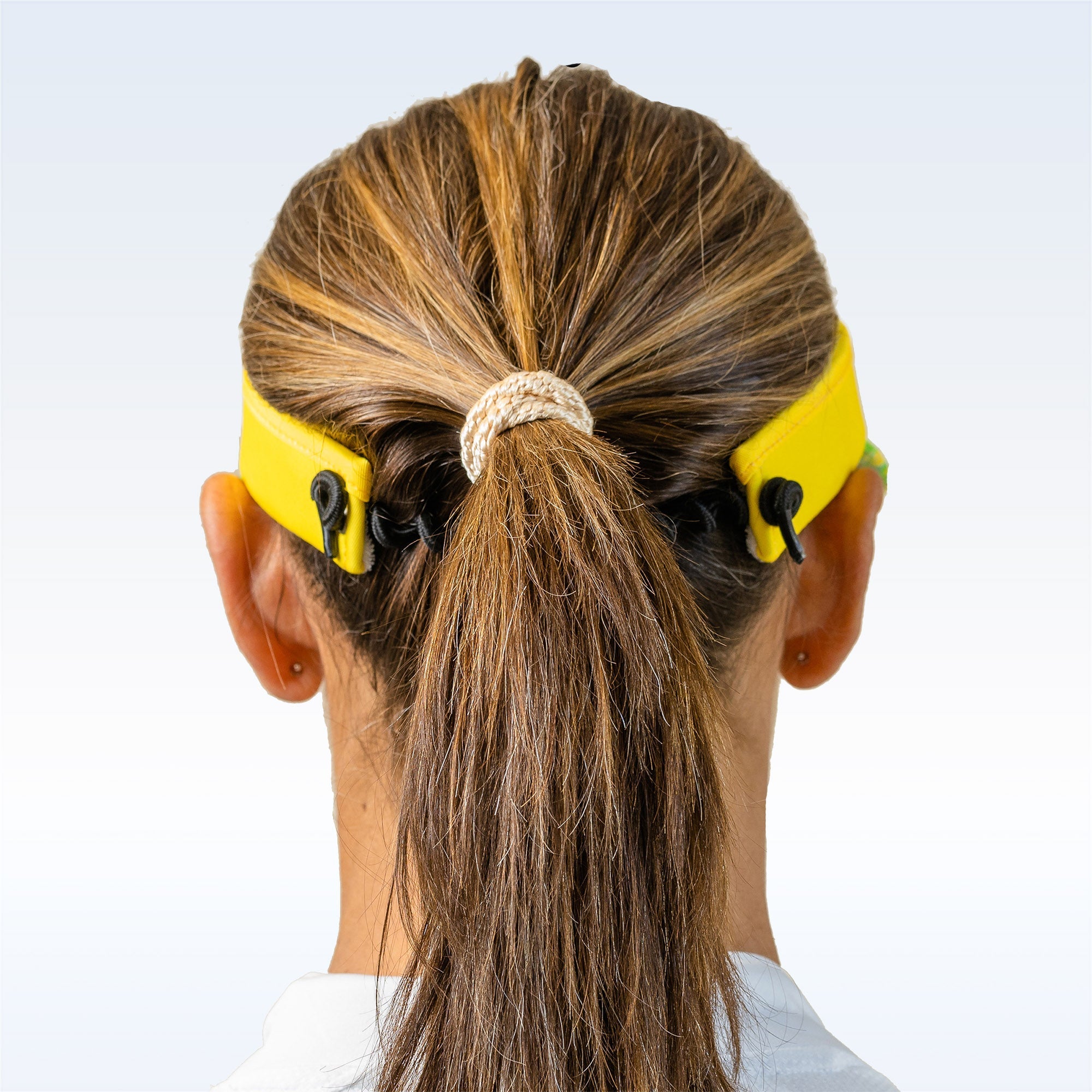Yellow visor by Pickleball Bella, worn from the back with black cord adjusters above a person's ponytail.