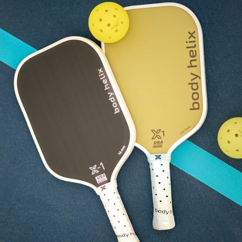 Two pickleball paddles and balls on a blue surface with a teal line.