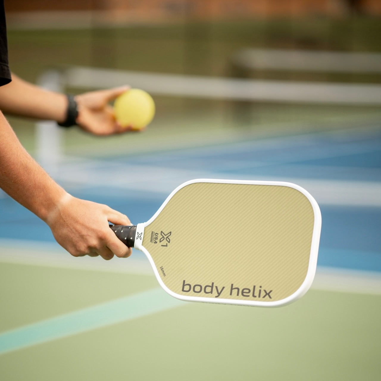 Person holding a pickleball paddle and a yellow ball on an outdoor court.