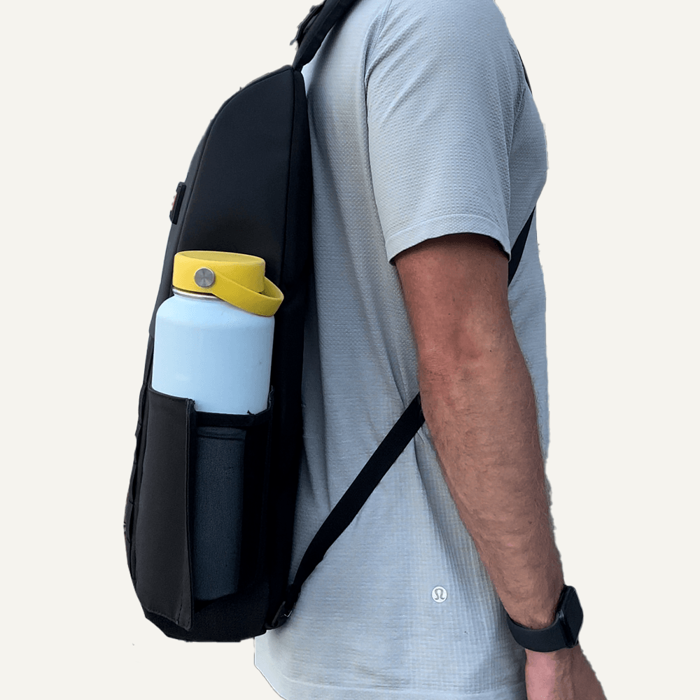A man wearing a grey shirt and a black backpack with a light blue water bottle.