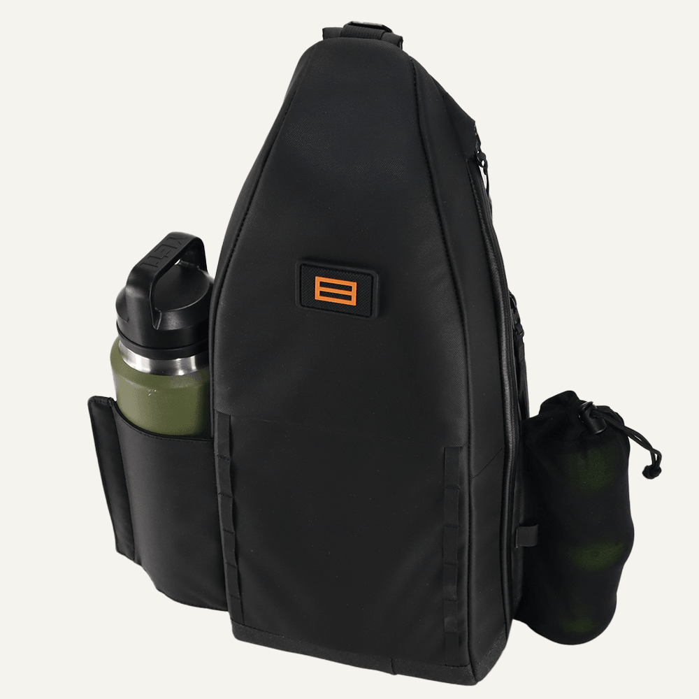Side view of a black pickleball sling by FORWRD featuring an orange logo patch, a grey water bottle, and a black drawstring pouch.