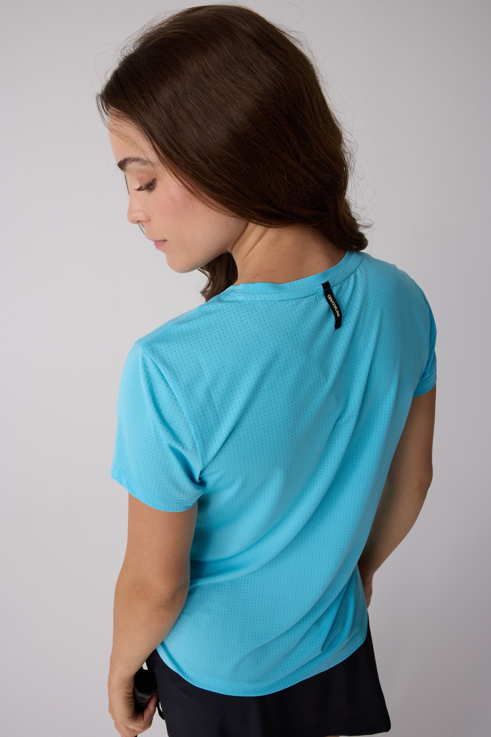 Blue perforated short sleeve women's tee by Centerline Athletics, seen from the back on a model wearing black shorts.