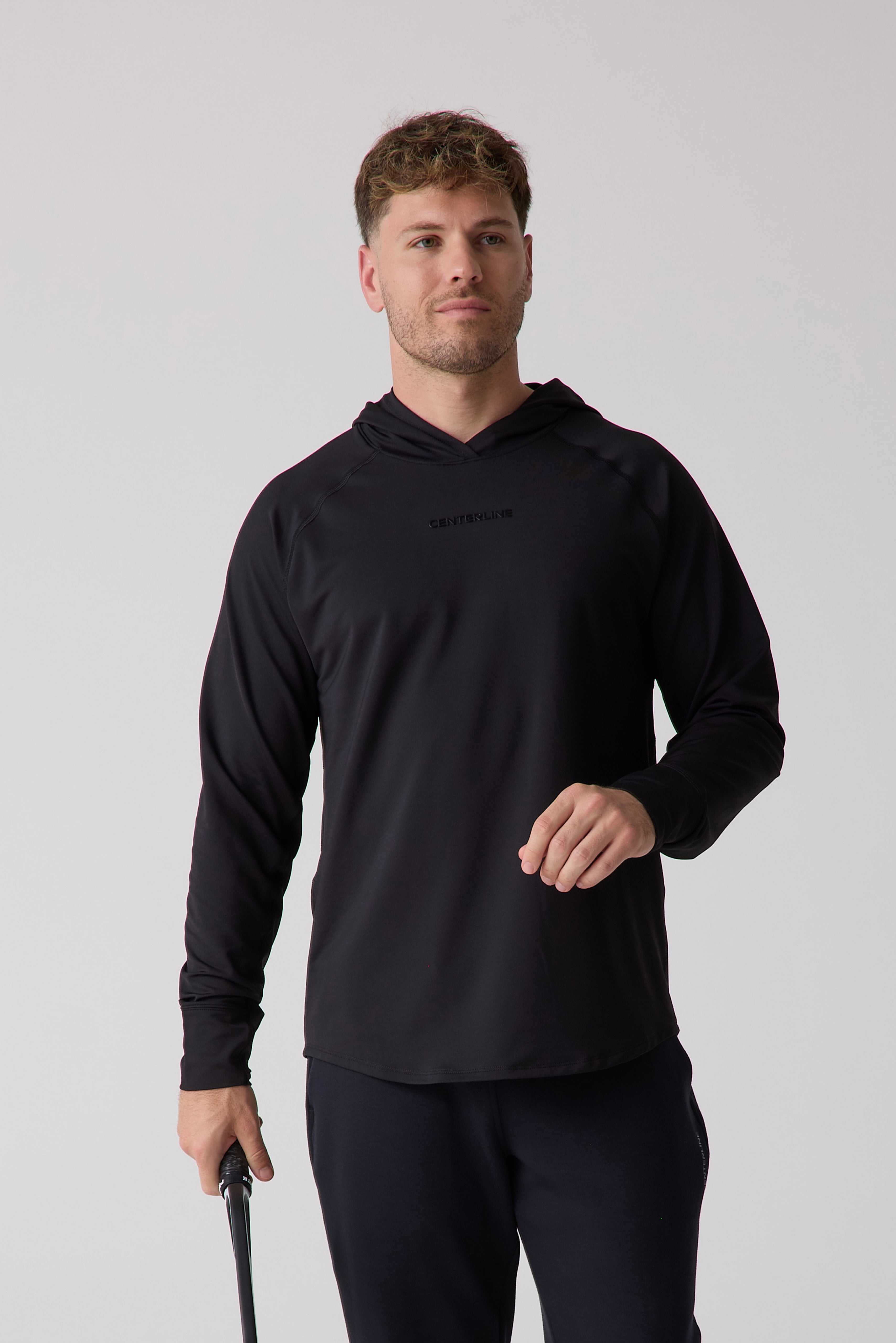 Black men's layering hoodie by Centerline Athletics with raglan sleeves and a subtle chest logo, worn by a man holding a tennis racket.