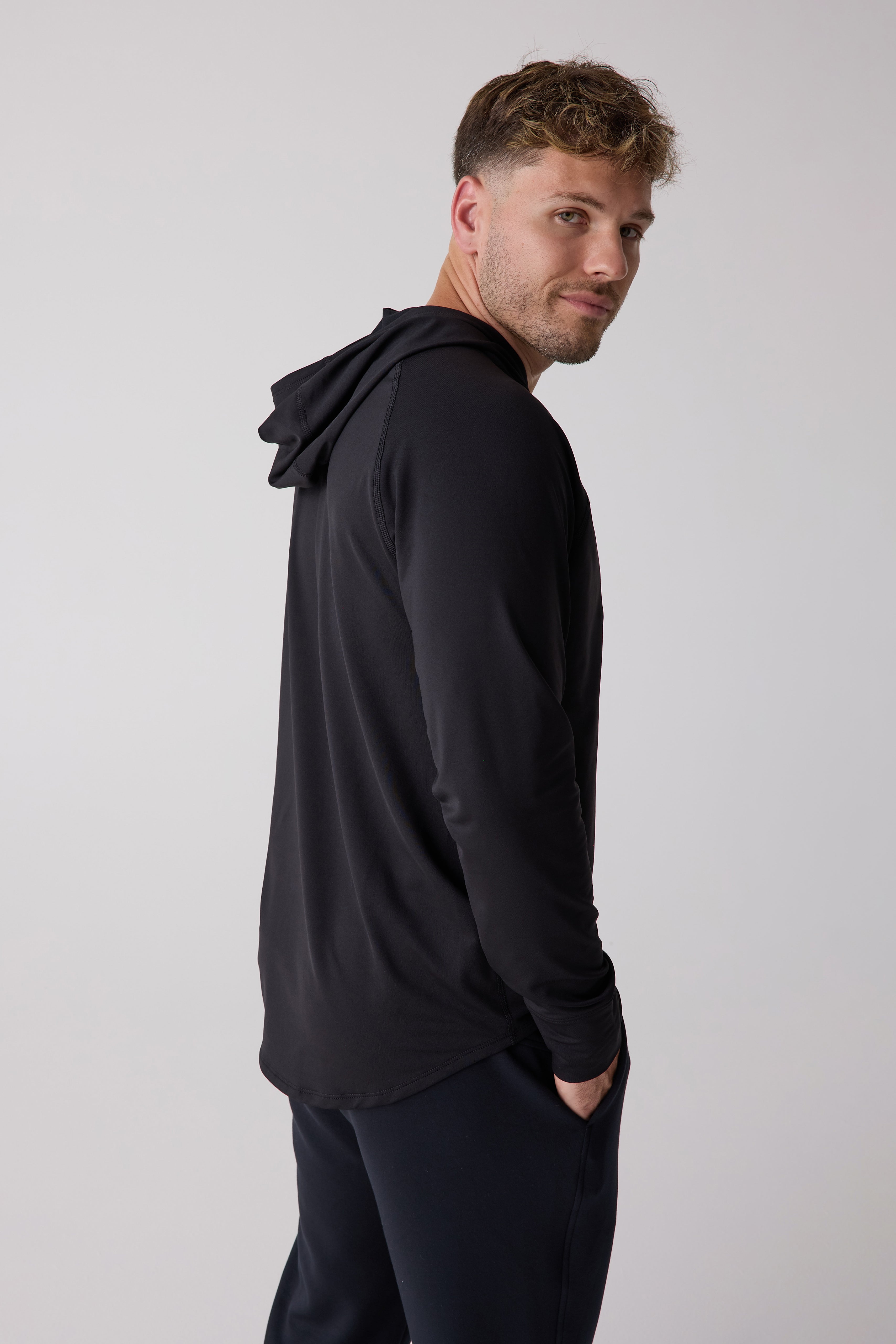 Black men's layering hoodie by Centerline Athletics with raglan sleeves, worn by a man looking over his shoulder.