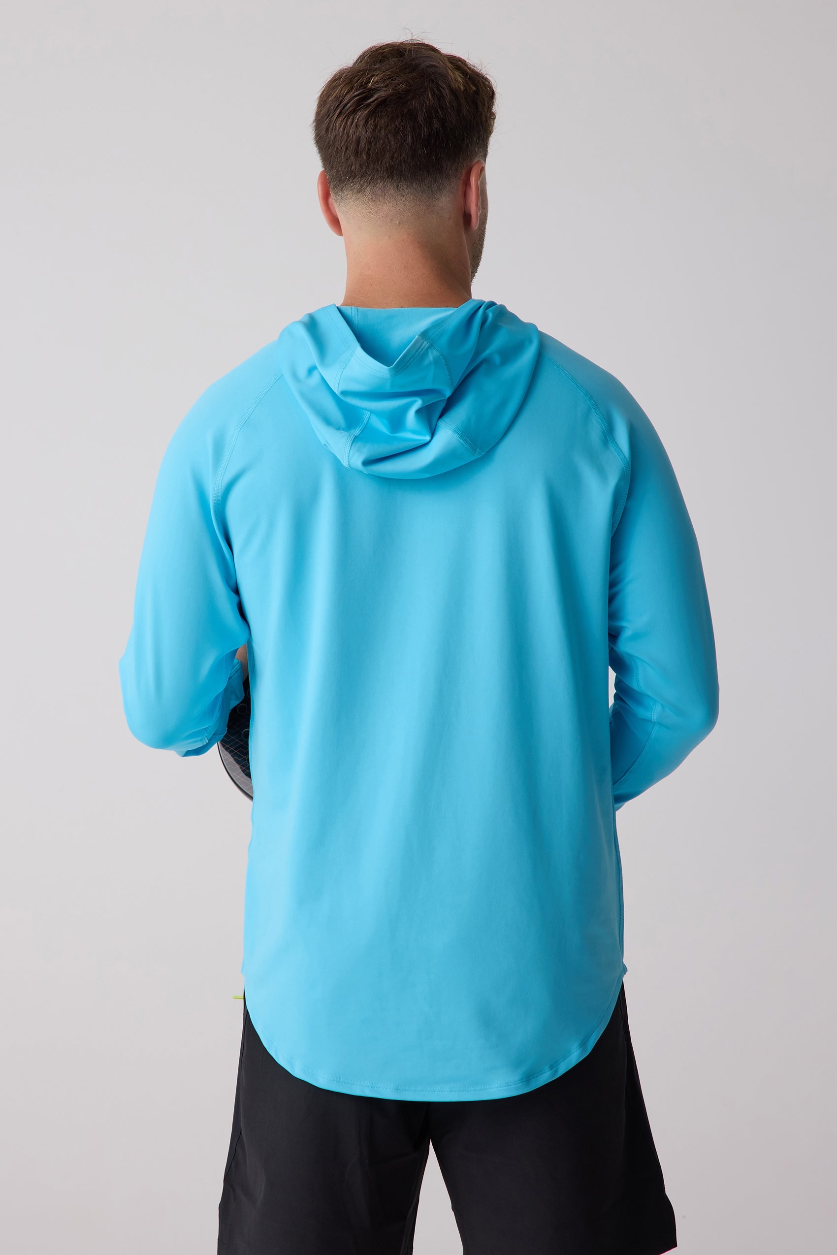 Bright blue men's layering hoodie by Centerline Athletics, shown from the back with long raglan sleeves and a rounded hem, worn with black shorts.