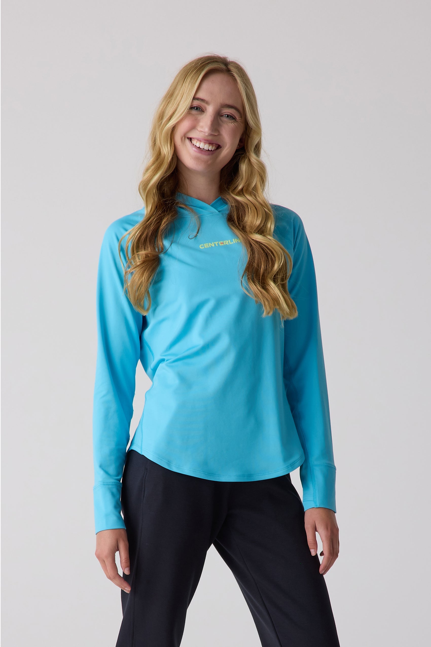 Women's blue layering hoodie by Centerline Athletics, with a chest logo, long sleeves, and a curved hem, worn with black pants.