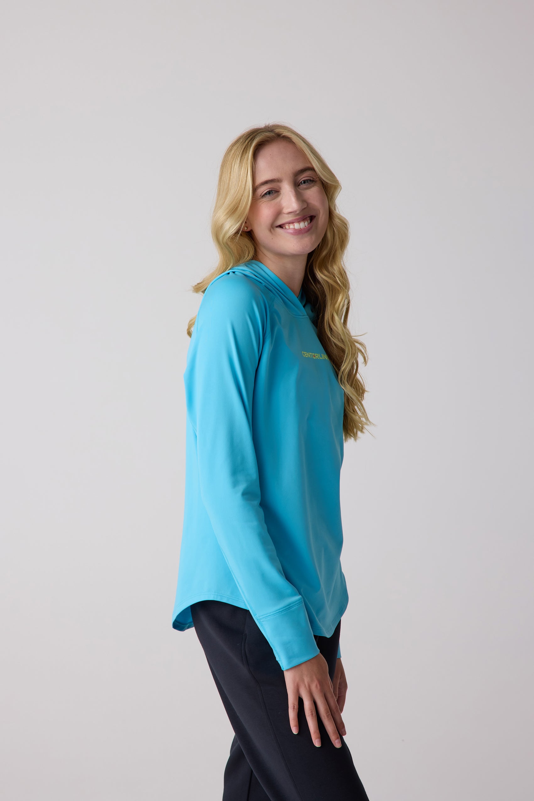 Vibrant blue women's layering hoodie by Centerline Athletics, featuring a subtle Centerline chest logo, worn by a smiling model in a side pose.